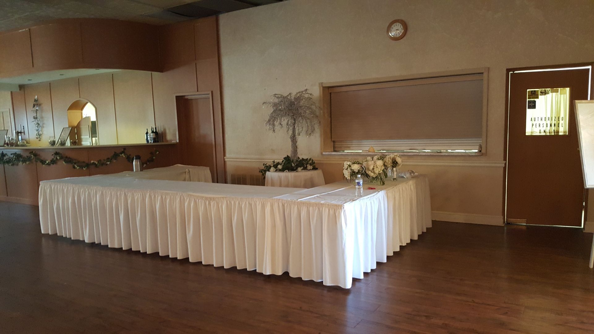 Banquet hall with a long white-draped table and wooden dance floor, set for an event.
