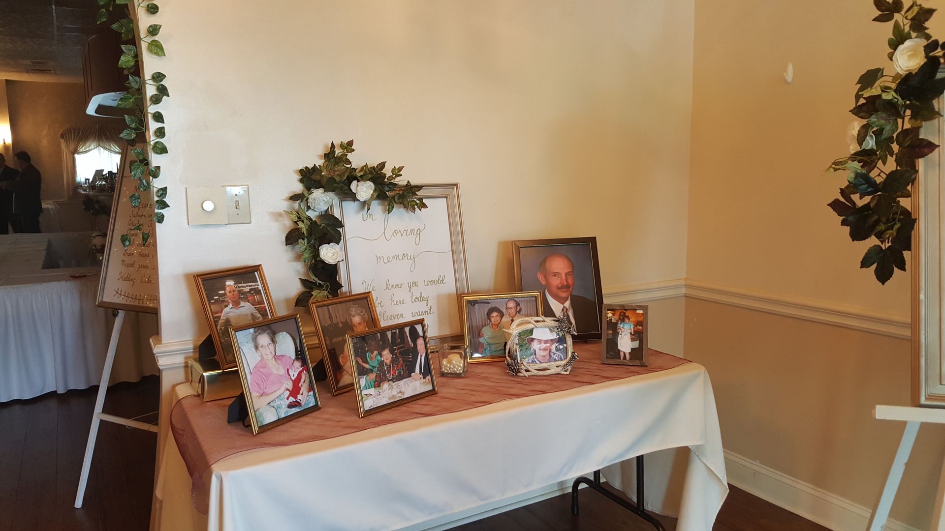 Memorial table with framed photos, flowers, and a portrait in a decorated indoor room