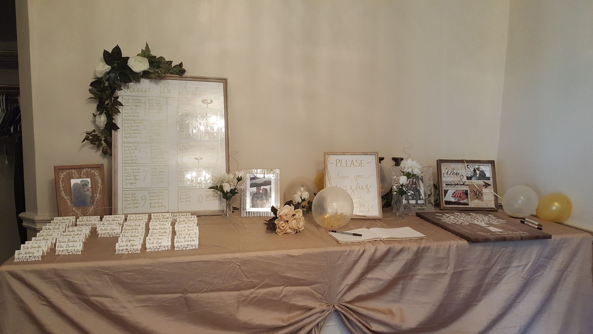 Decorated memorial table with framed photos, flowers, candles, and folded cards on a beige draped cloth.