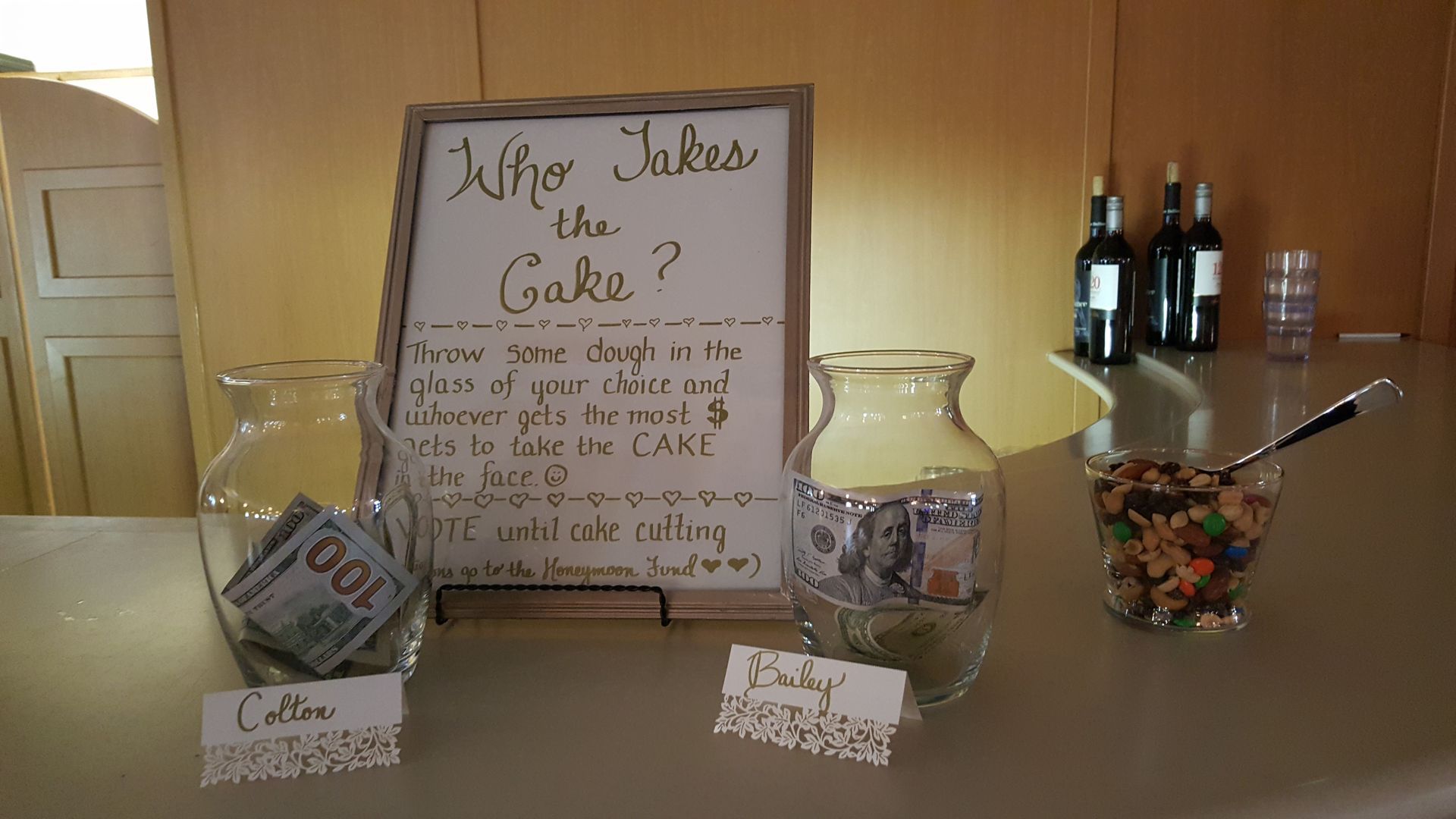 Mason jar donation display with “Who Took the Cake?” sign, cash jar, candy jar, and wine bottles on a counter