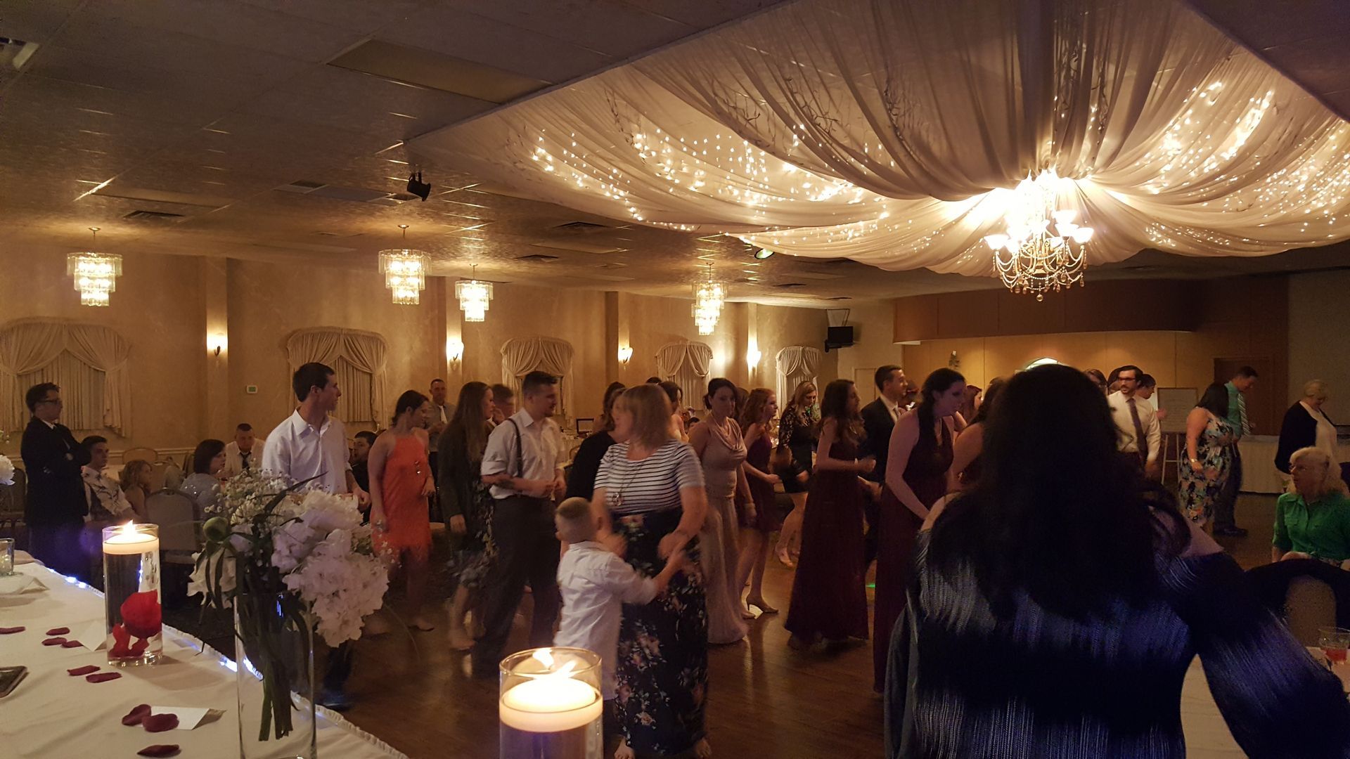 Guests dancing at a warmly lit indoor reception with draped ceiling decorations and candles