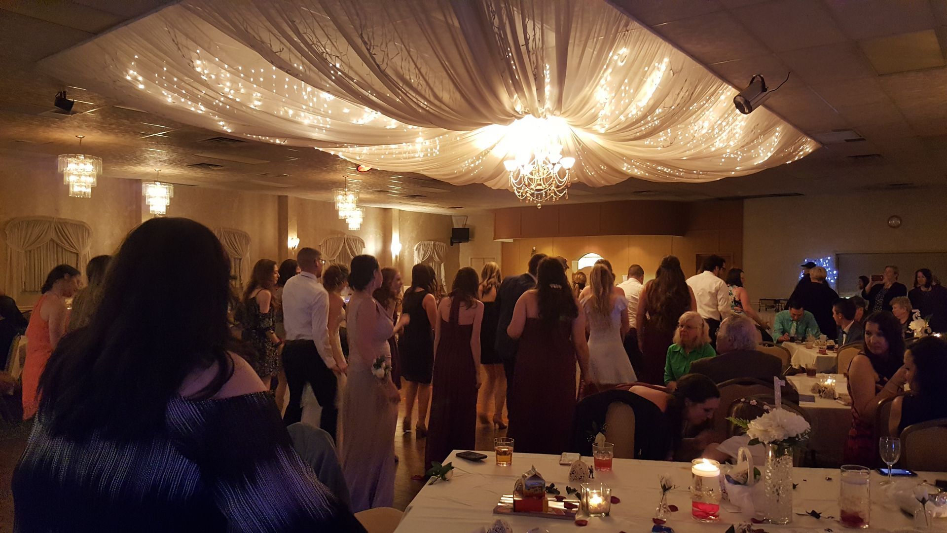 Guests mingling at a warmly lit banquet hall with draped ceiling and tables set for a formal event