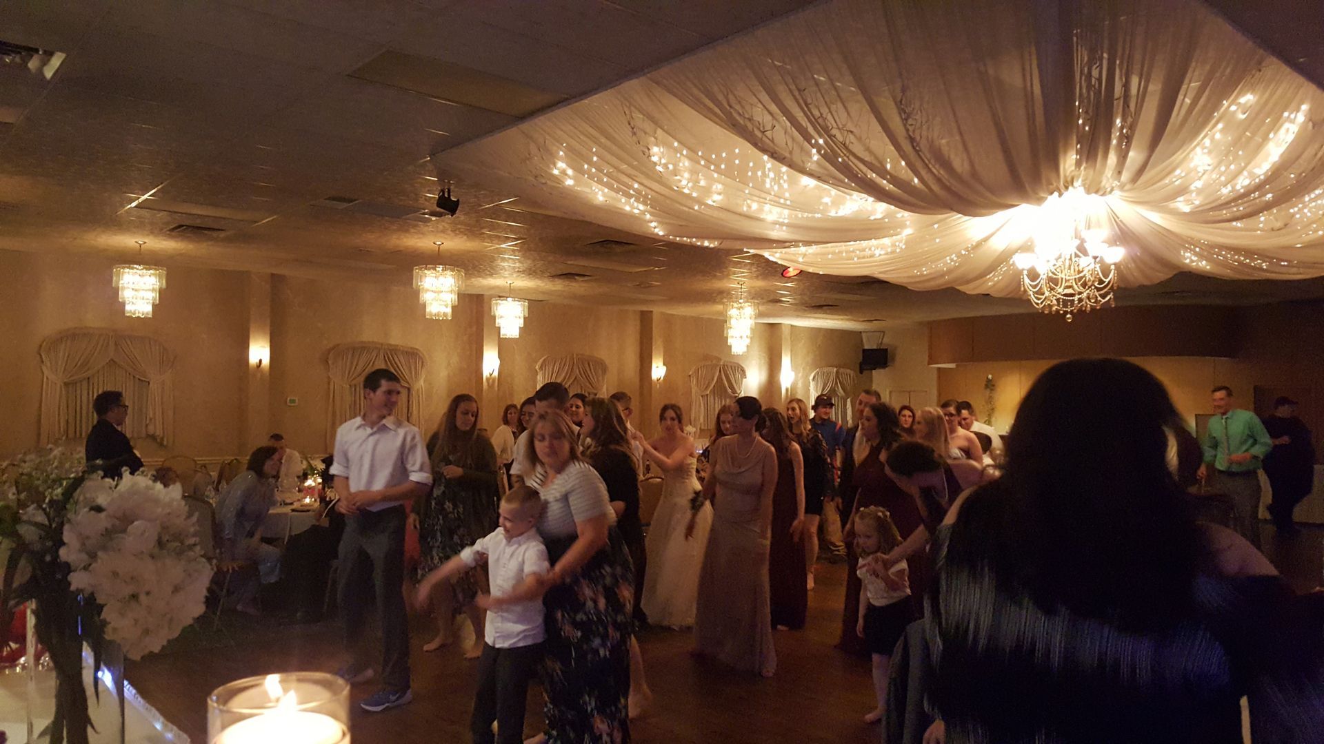 Guests dancing at a warmly lit indoor reception with draped ceiling and string lights