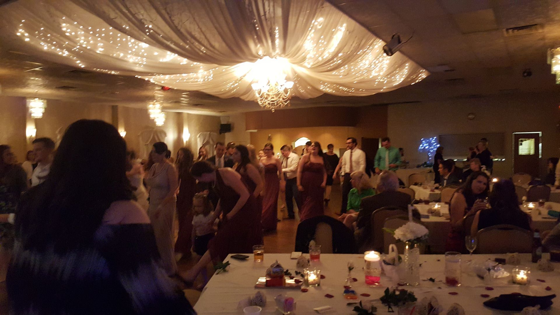 Guests mingling at a warmly lit banquet hall with draped ceiling fabric and decorated tables