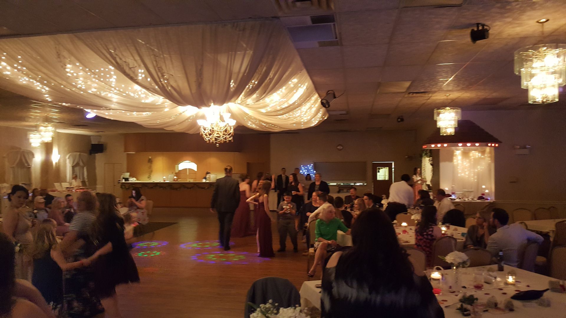 Reception hall with draped ceiling lights and guests mingling and dancing on the floor