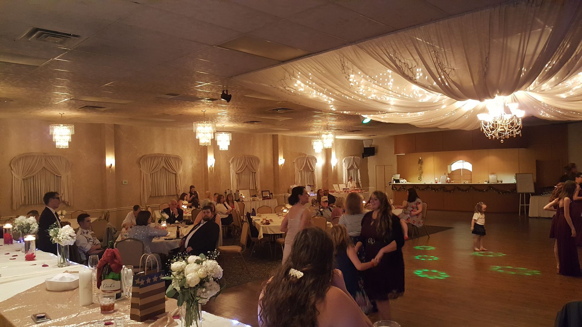 Guests dancing at a warmly lit banquet hall with draped ceilings and tables set around the floor