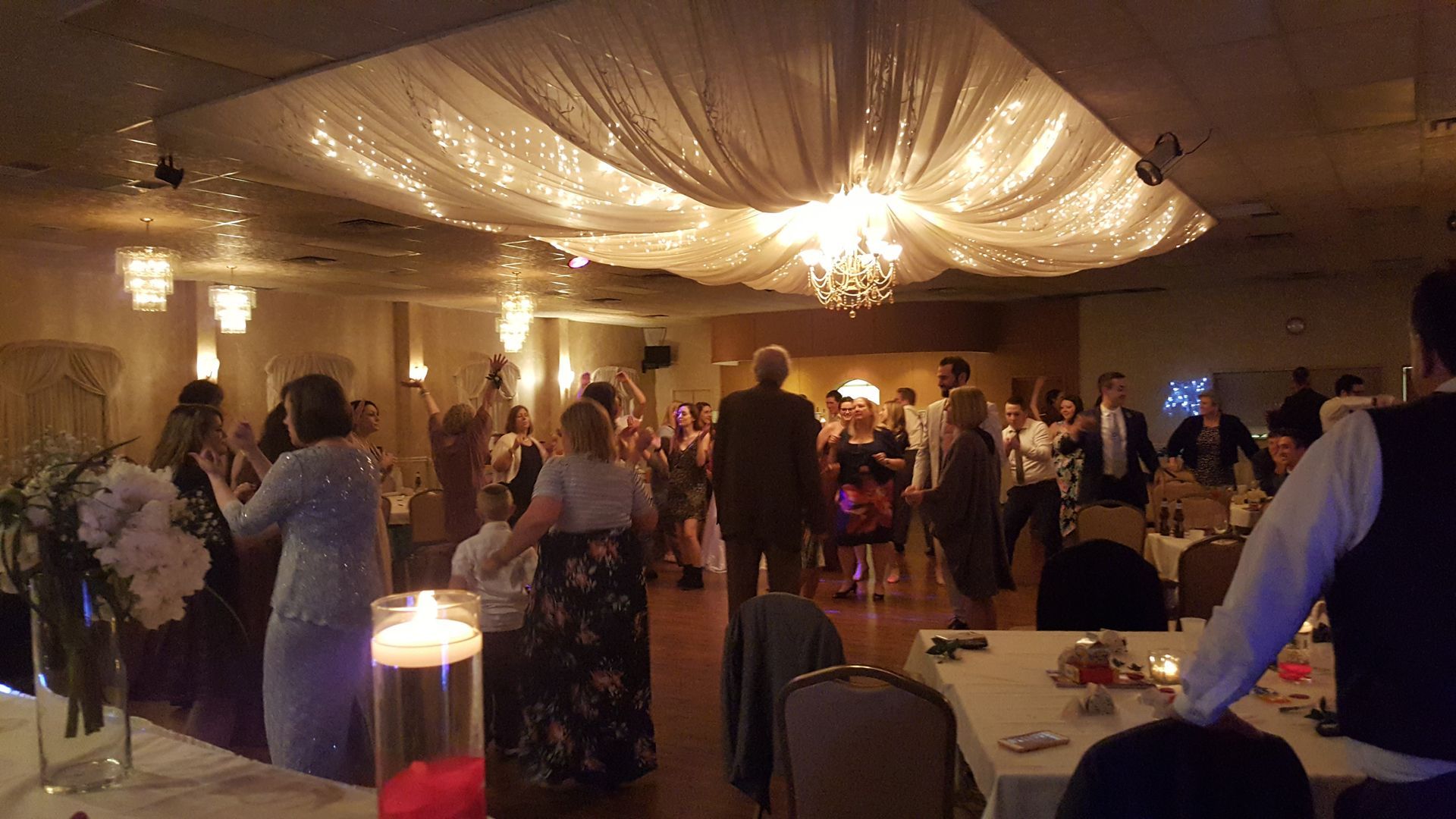 Decorated banquet hall with guests mingling under draped ceiling lights and chandeliers
