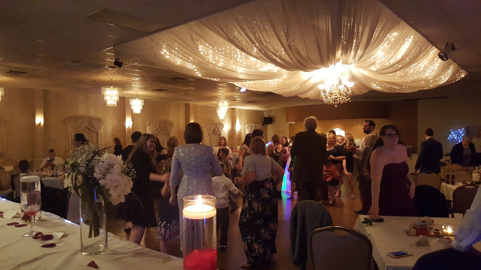 Guests mingling at a warmly lit indoor banquet with draped ceiling decor and tables