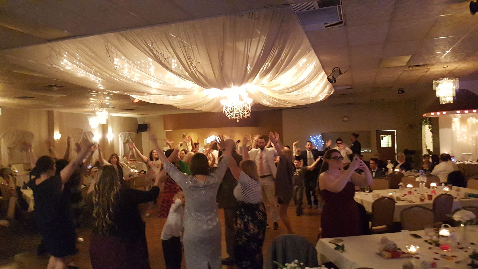 Guests dancing under draped ceiling lights at a warmly lit banquet hall reception