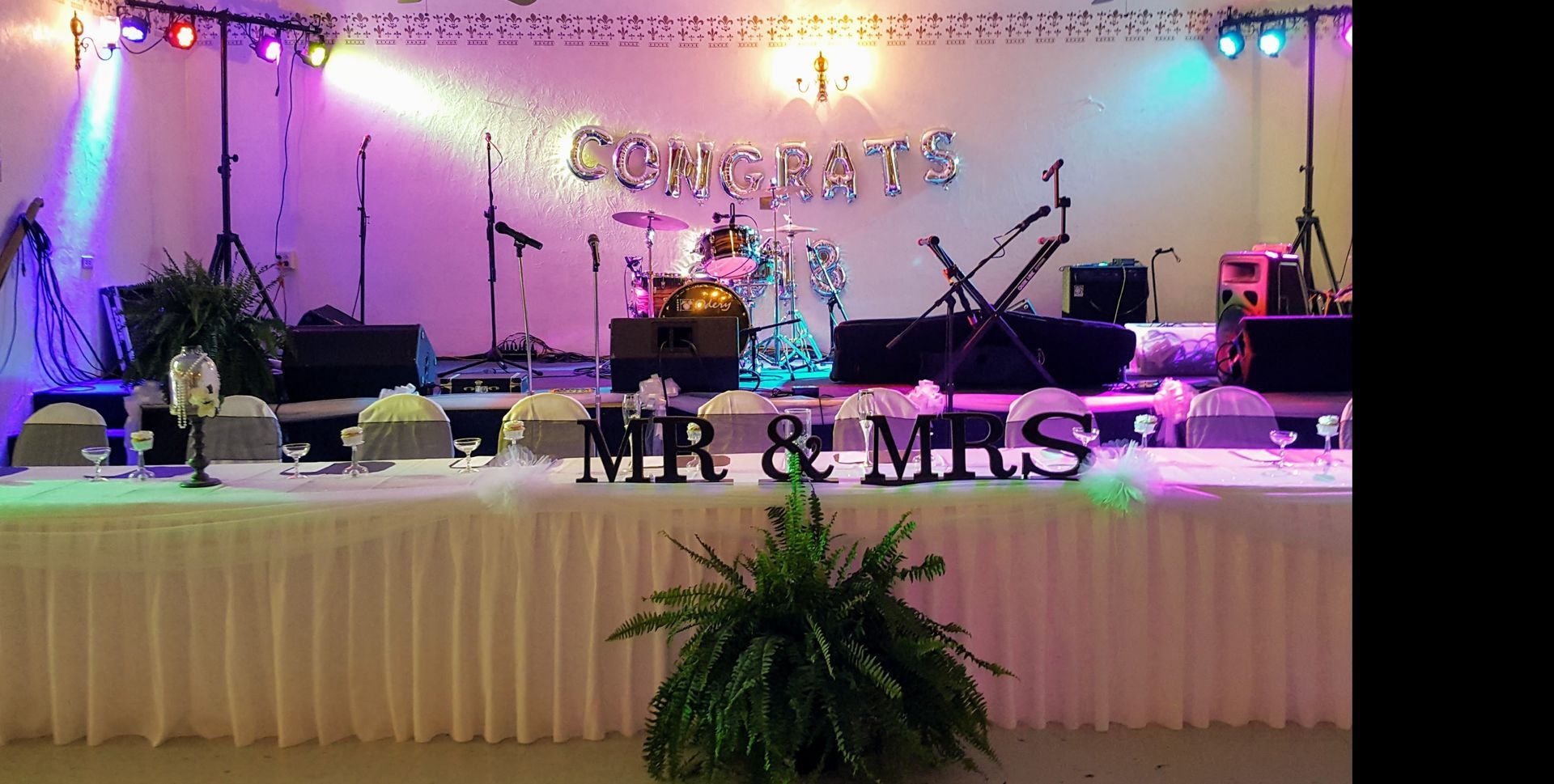 Decorated wedding stage with lights, floral accents, and “MR & MRS” sign on the front table