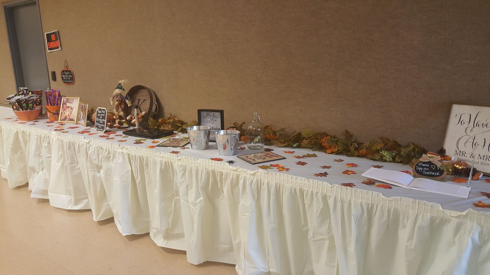Decorated banquet table with white tablecloth, autumn leaves, photos, and assorted items on display