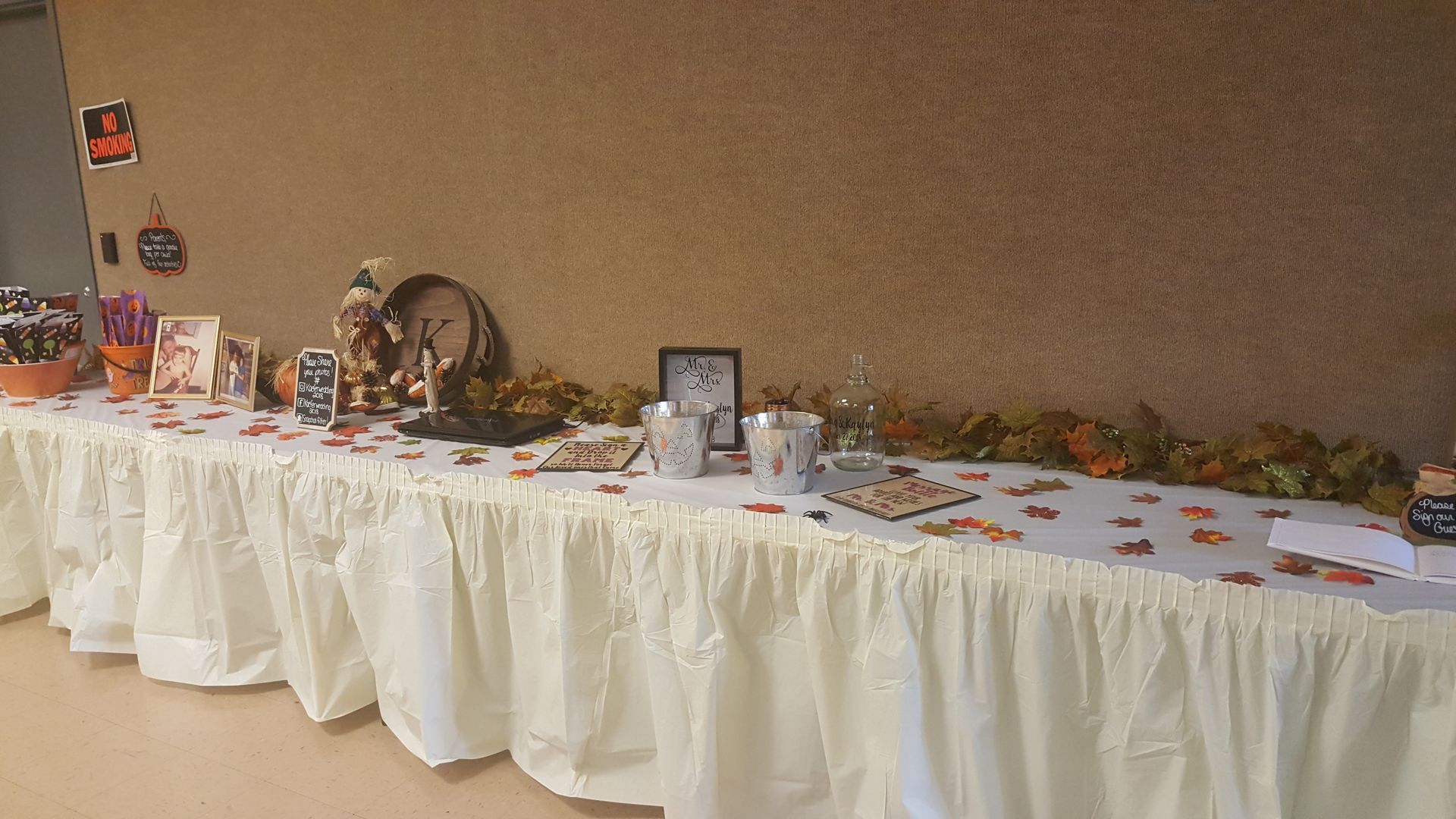 Long banquet table with white skirting and autumn decor against a beige wall
