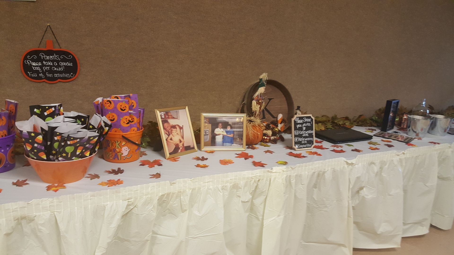 Decorated dessert table with Halloween-themed treats, photos, and signs on a white tablecloth