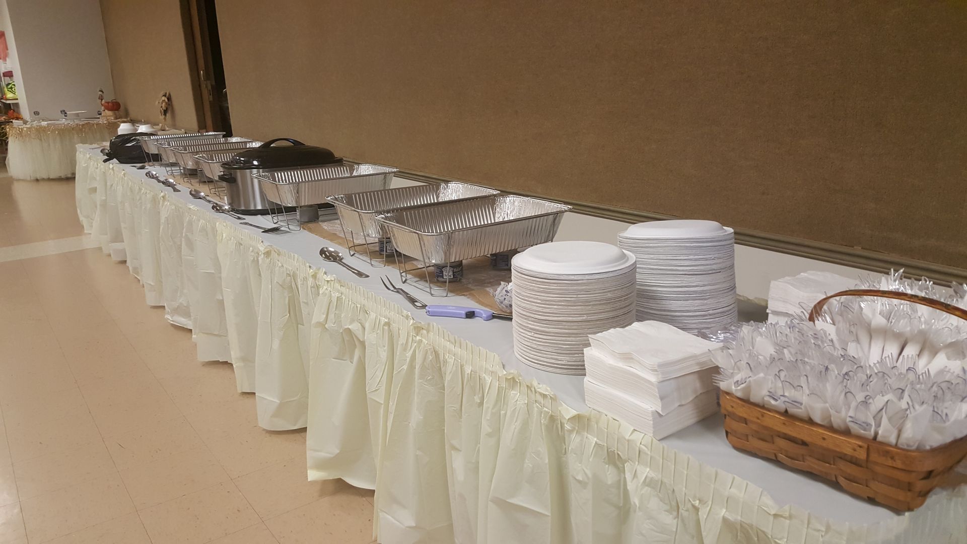 Buffet table with covered dishes, stacks of white plates, and rolls in a banquet room