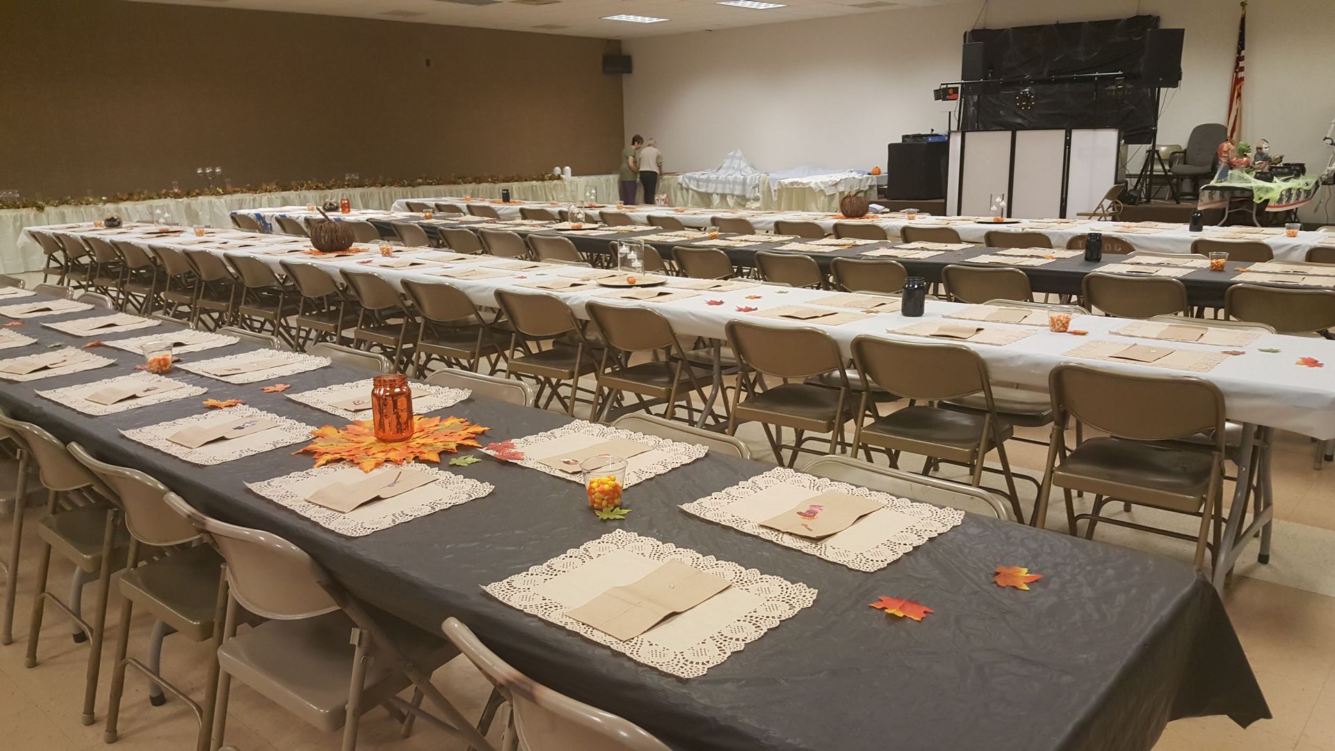 Conference room with long tables, folded chairs, white placemats, and orange table decorations.
