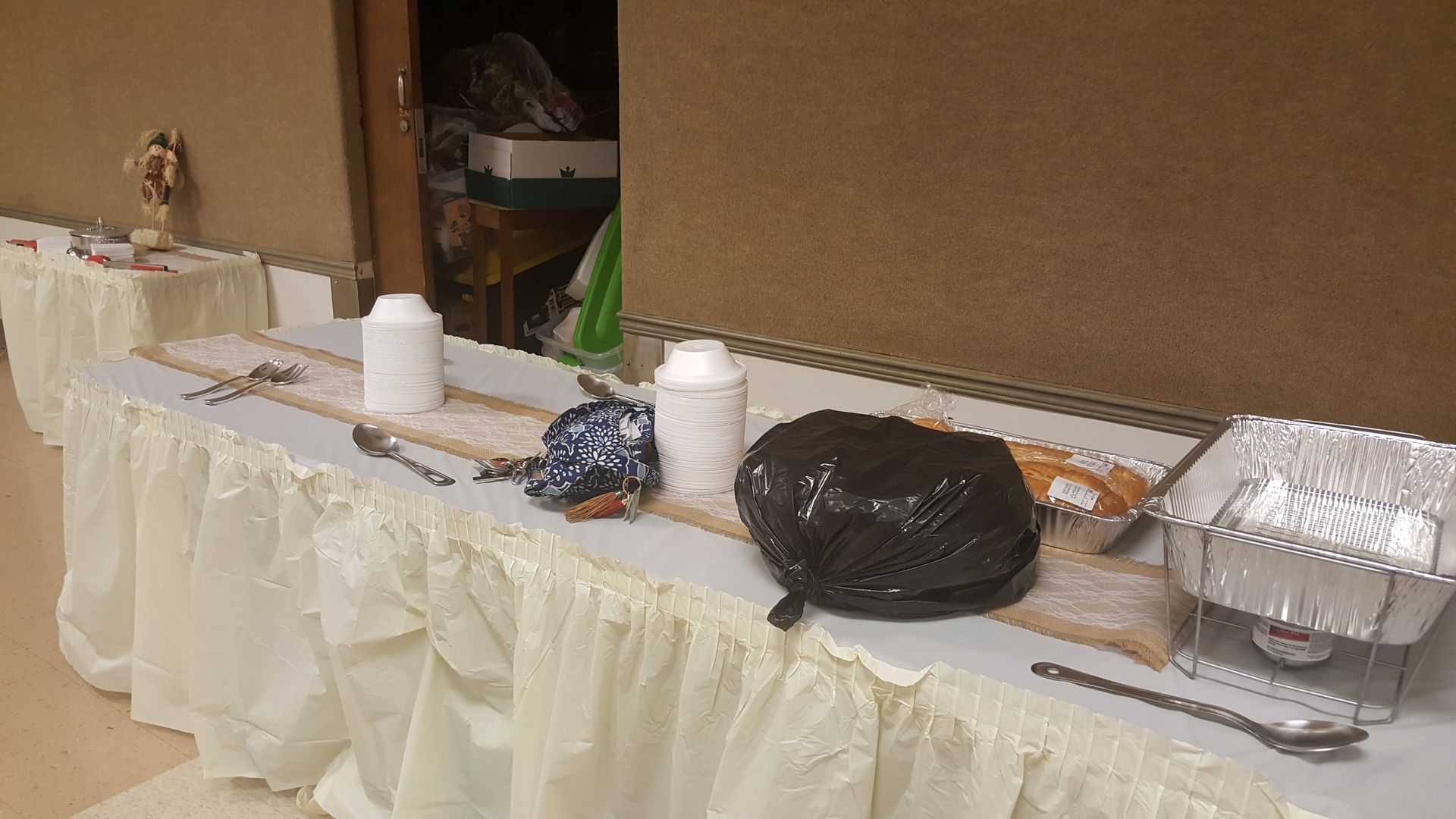 Buffet table with food trays, coffee cups, plates, and foil-covered dishes against a tan wall.