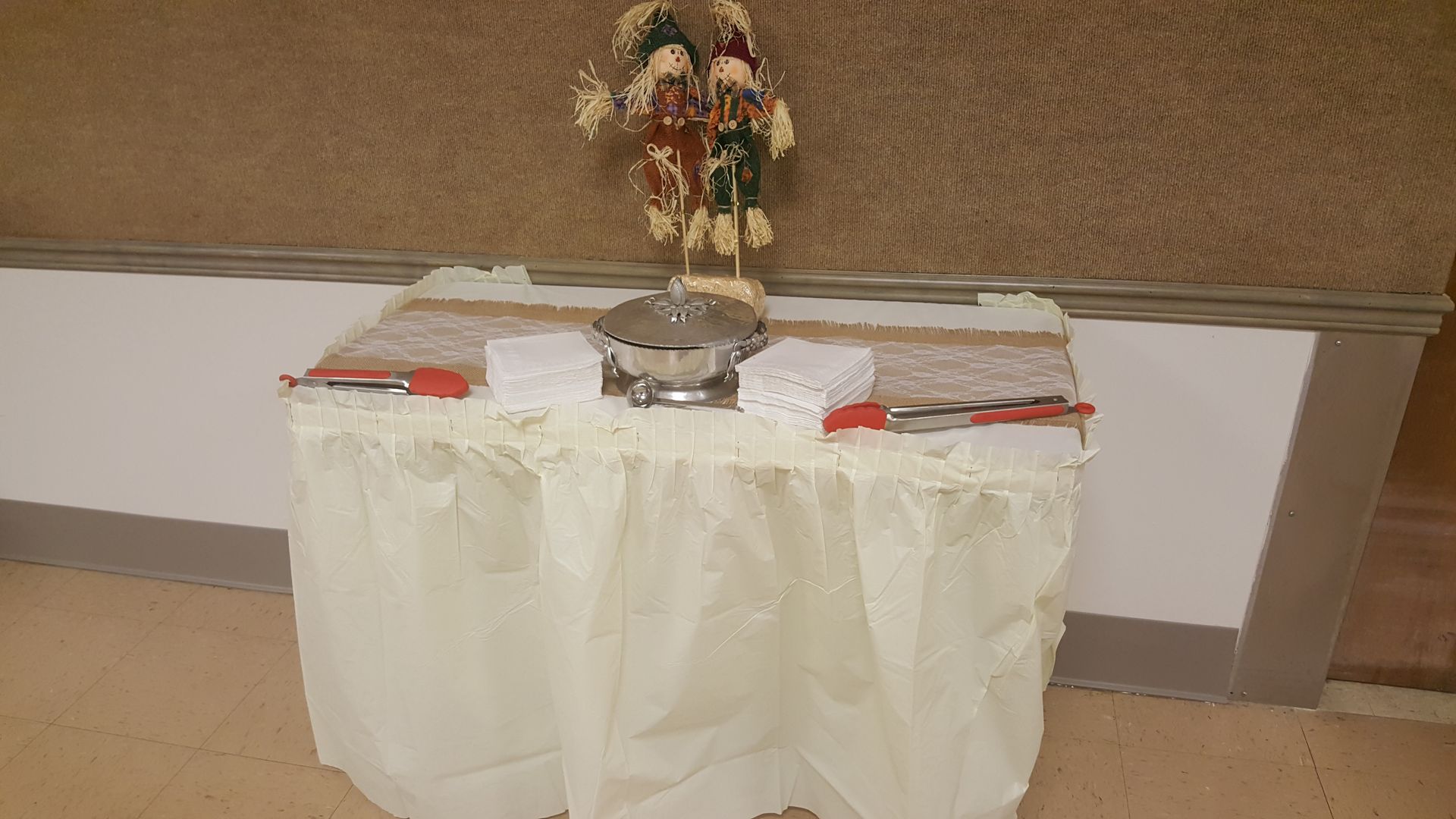 Decorated table with floral centerpiece and red napkins against a tan wall in a banquet hall