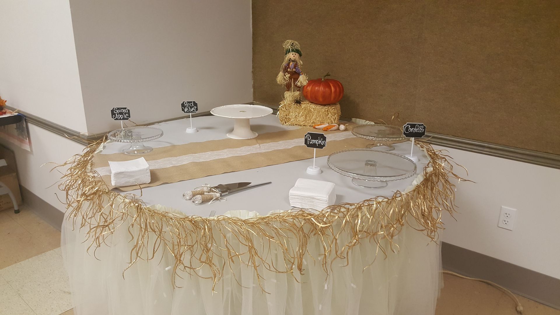 Decorated banquet table with white tablecloth, gold garland, pumpkins, plates, and a fall centerpiece