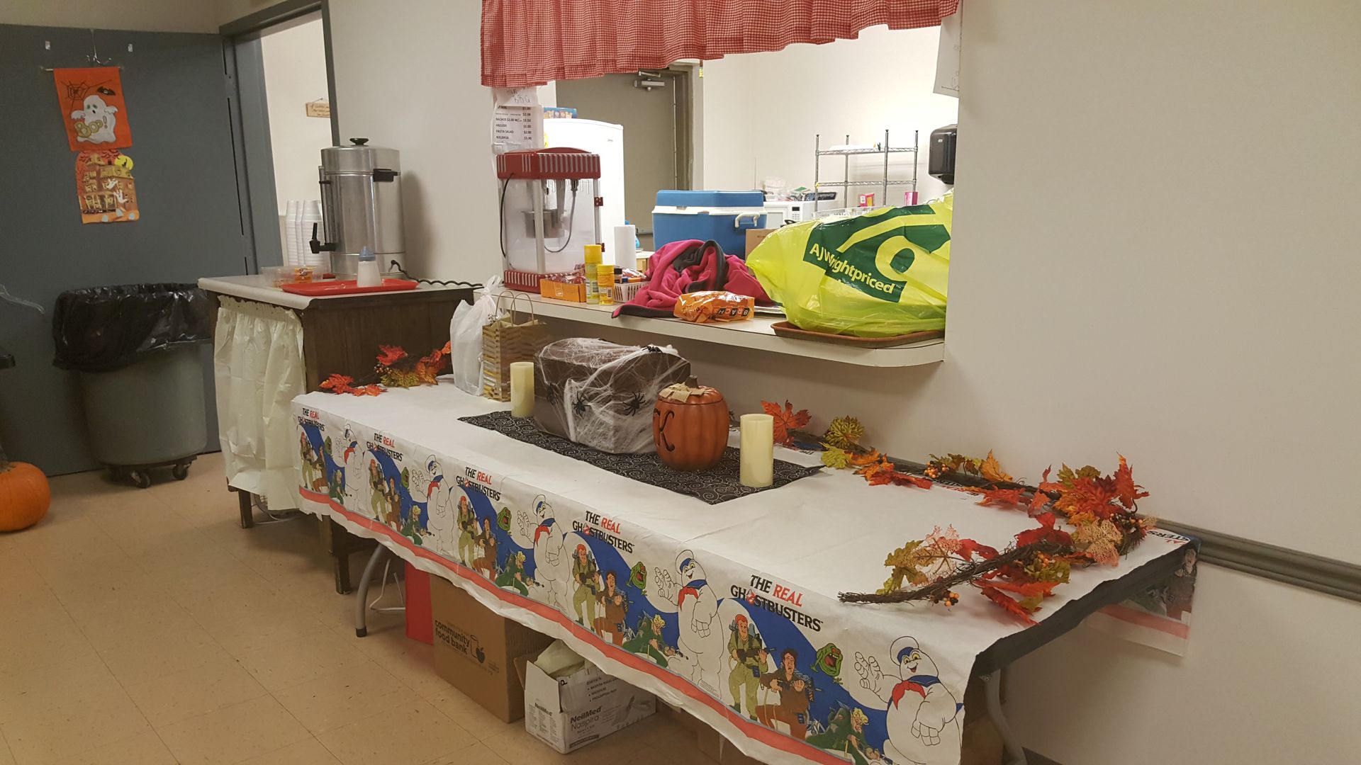Decorated buffet table with snacks and drinks in a community room, with fall garland and a trash bin nearby