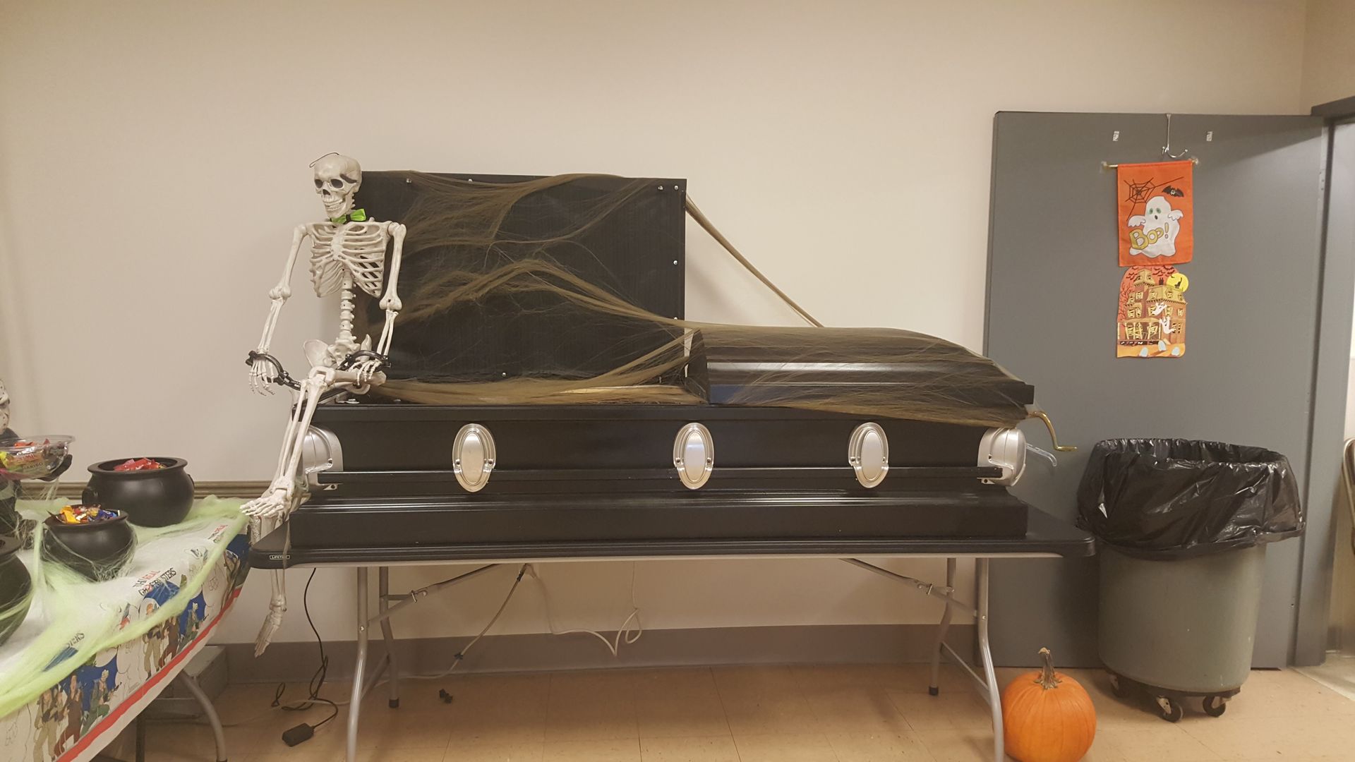 Black coffin on a metal table in a room, with a silver garland and orange pumpkin nearby.