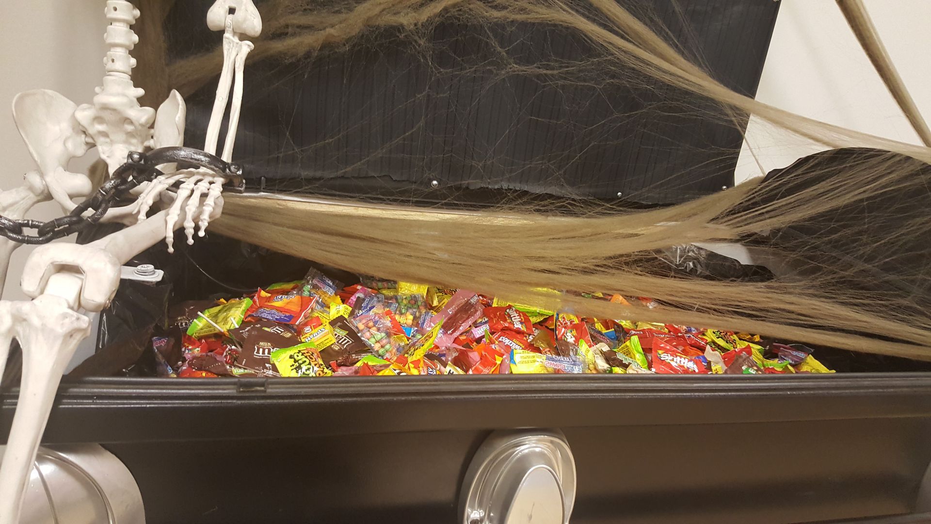 Skeleton figure lounging beside a black tray filled with colorful candy under a spiderweb decoration