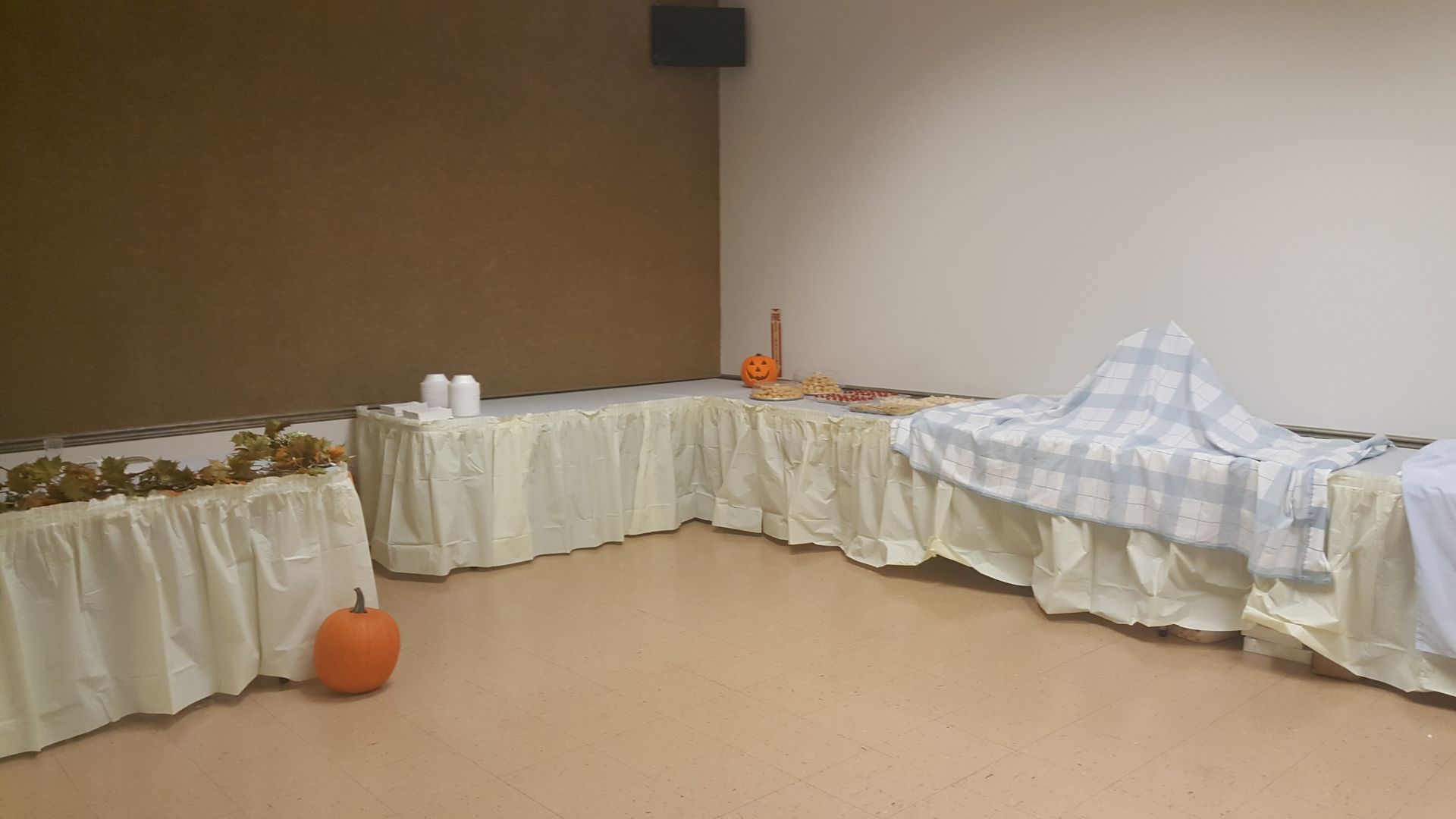 Small decorated room with white-draped tables along the walls and pumpkins on the floor.