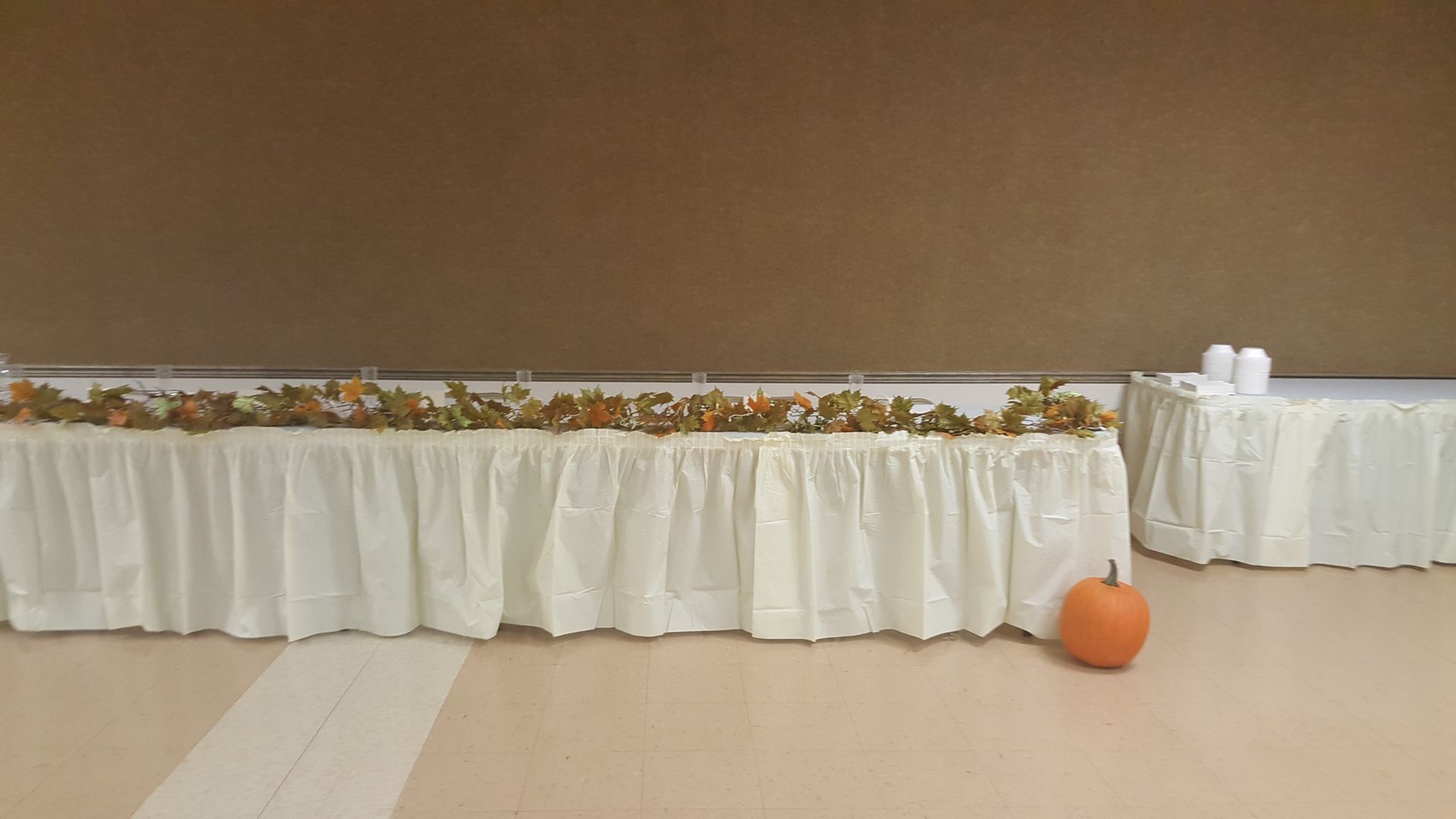 Decorated banquet table with white tablecloth, autumn garland, and an orange pumpkin on the floor
