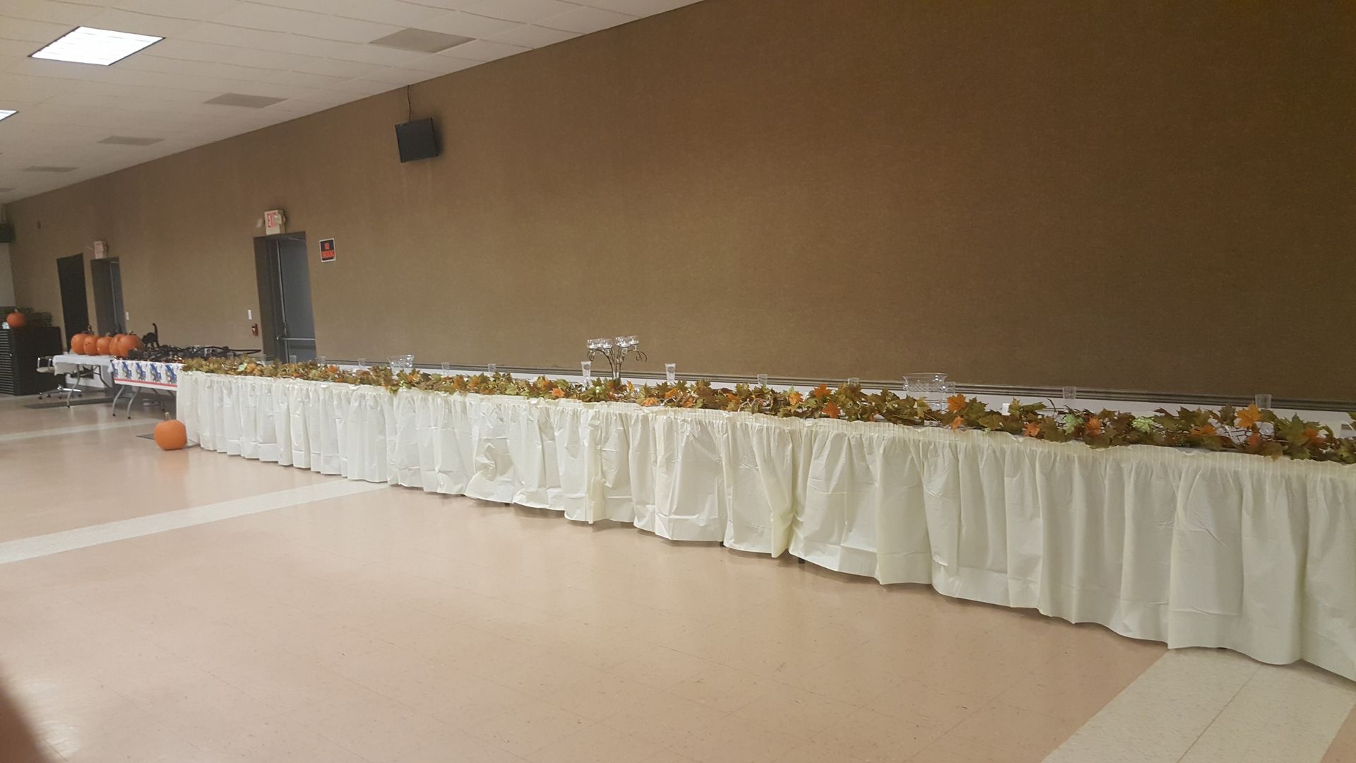 Long buffet tables with white tablecloths lined against a beige wall in a banquet hall