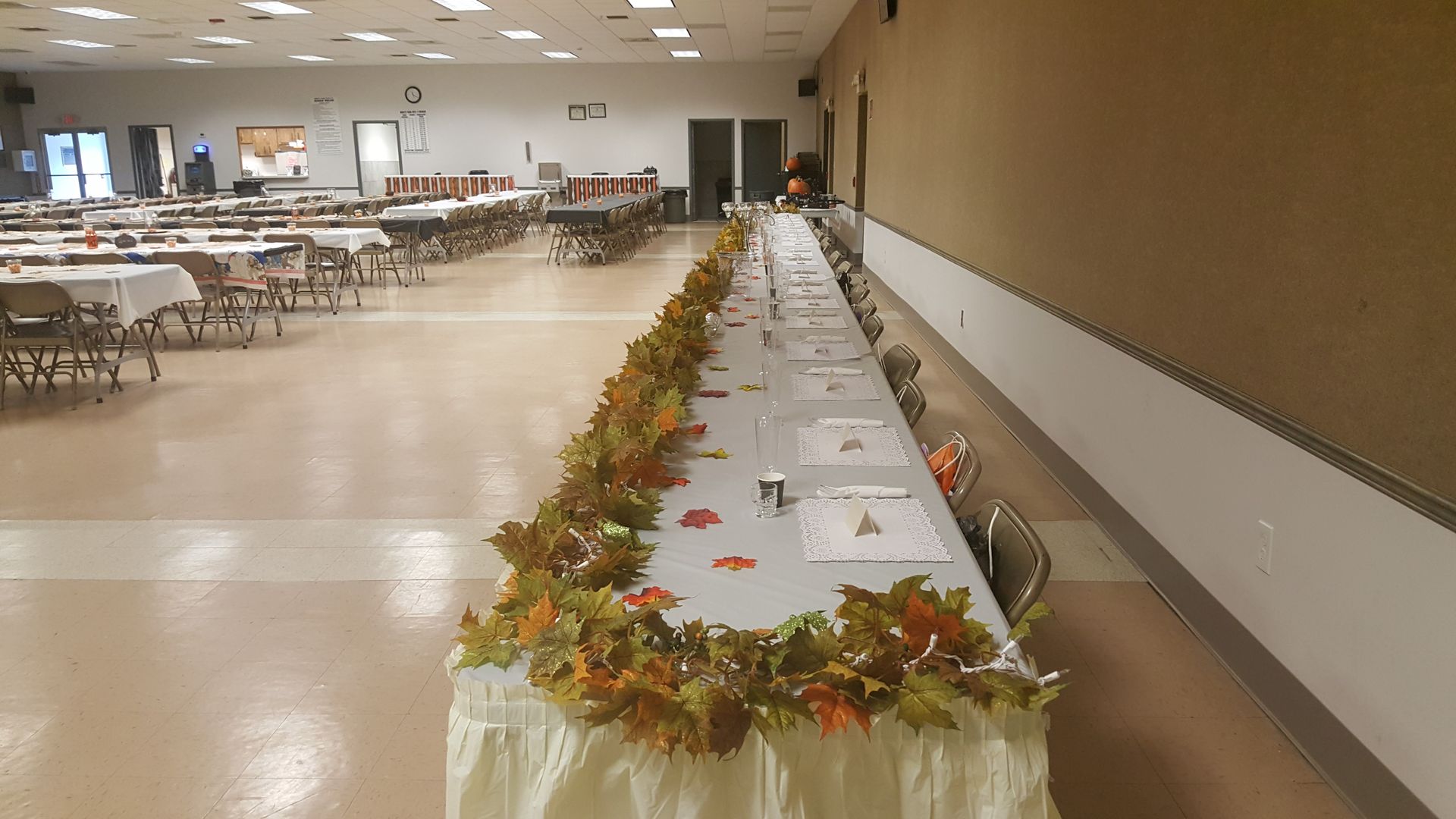 Long banquet table with autumn garland in a large empty hall