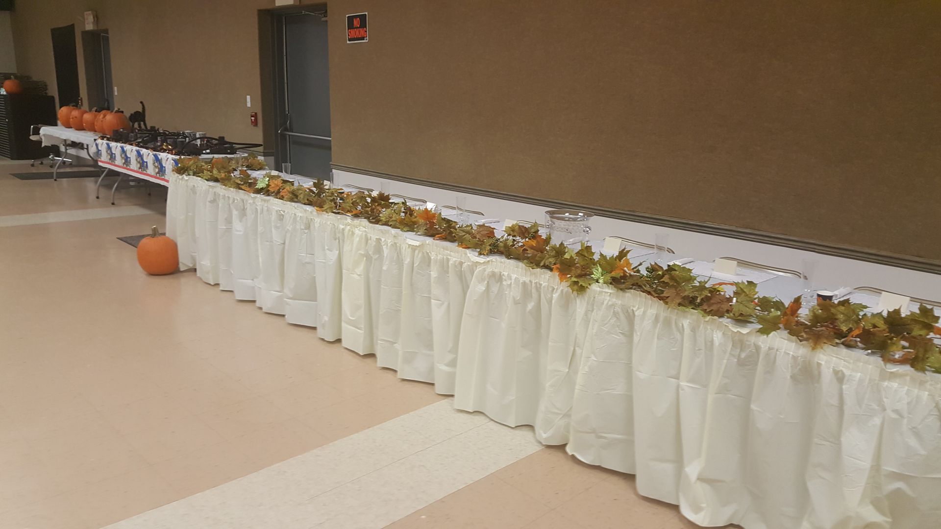 Long banquet table with white tablecloths and autumn centerpieces in a hallway.