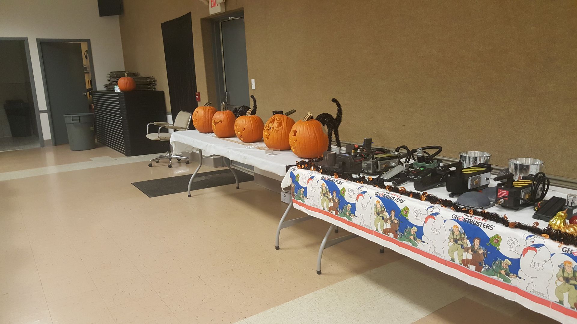 Table with pumpkins and toy vehicles arranged in a room, with Halloween decorations and a tablecloth.
