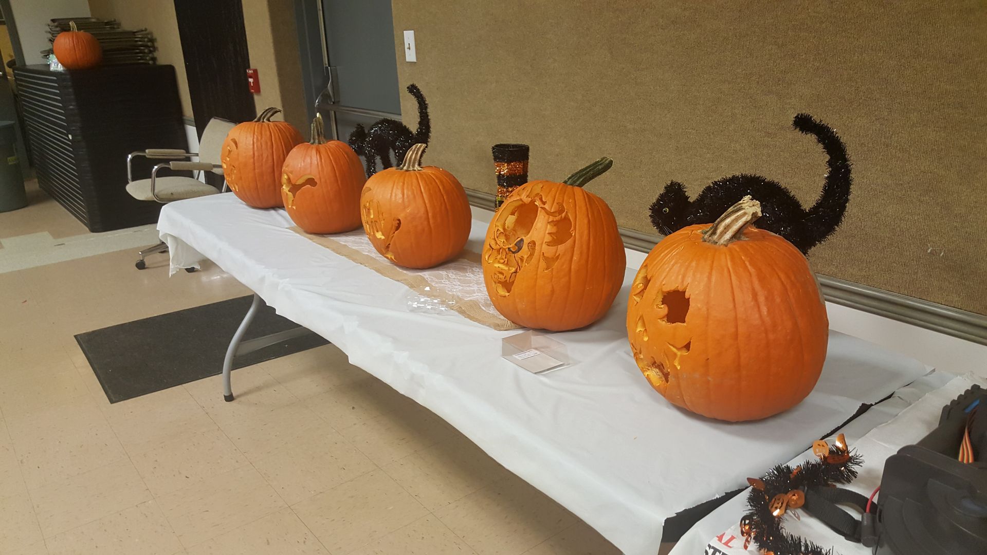 Carved pumpkins on a white table at a festive outdoor display, with a decorative black cat nearby