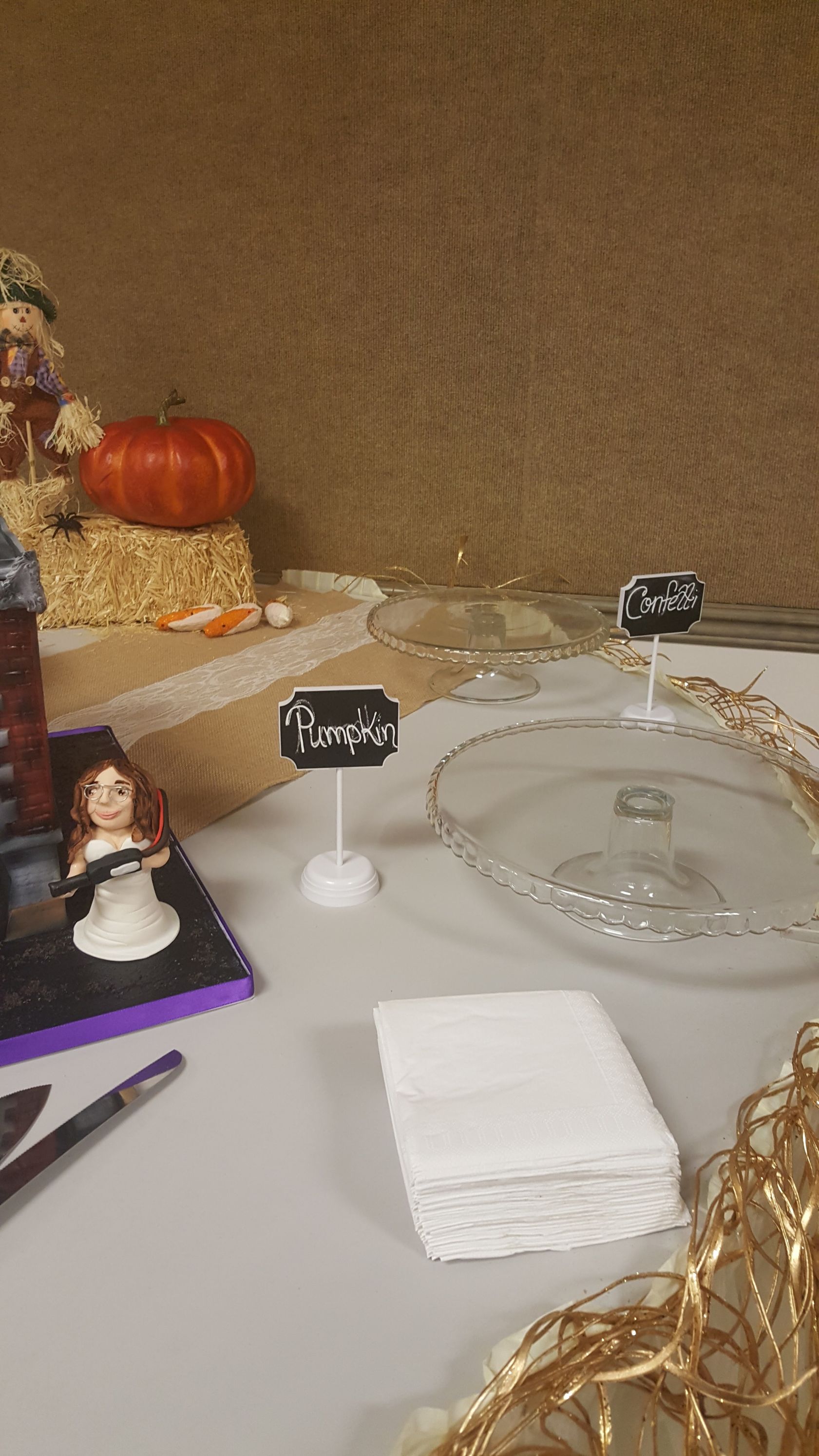 Halloween-themed table with pumpkin decor, small figurines, and stacked white napkins on a white surface