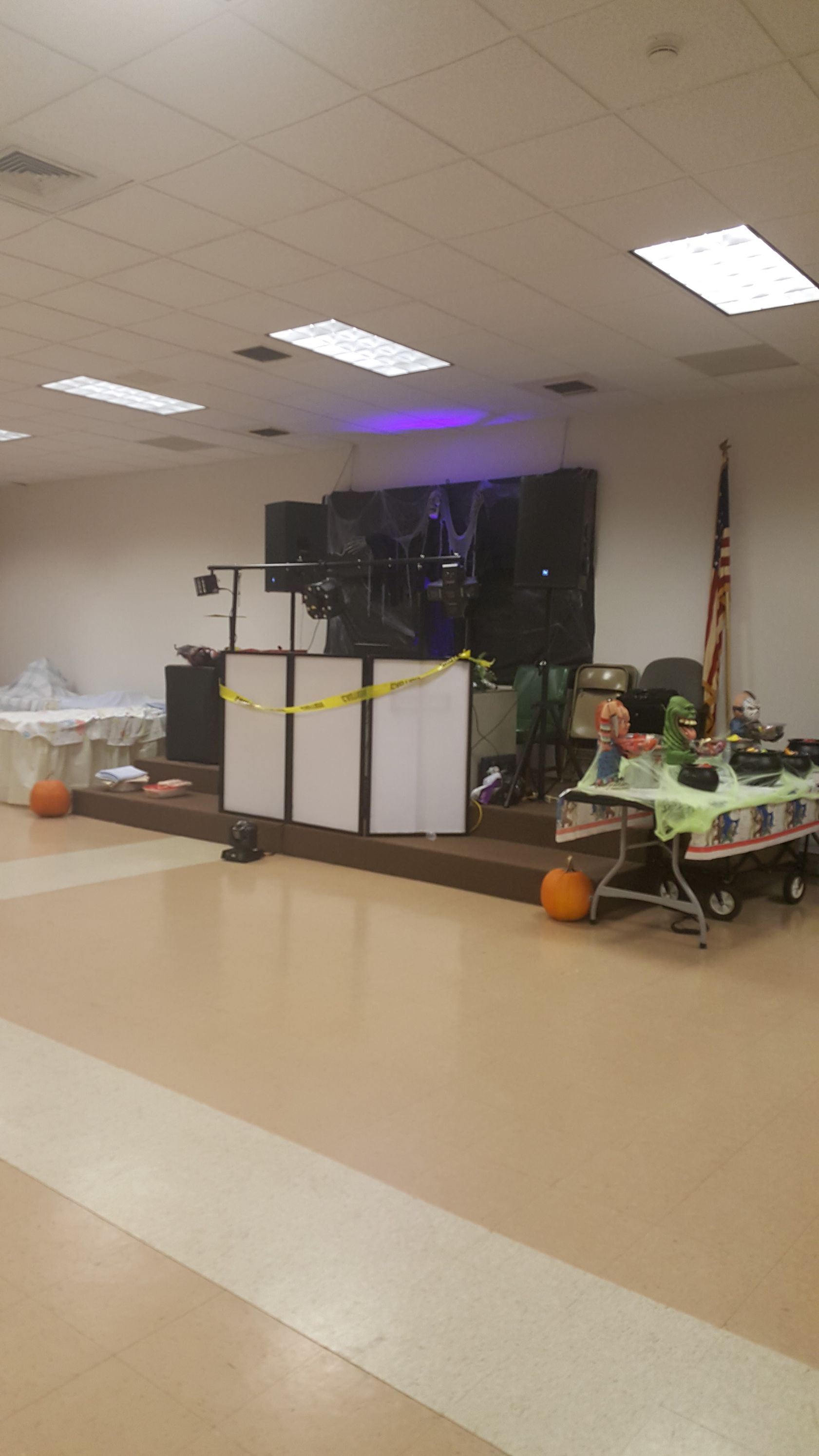 Decorated classroom with Halloween-themed display tables, pumpkins, and purple lights under a tiled ceiling