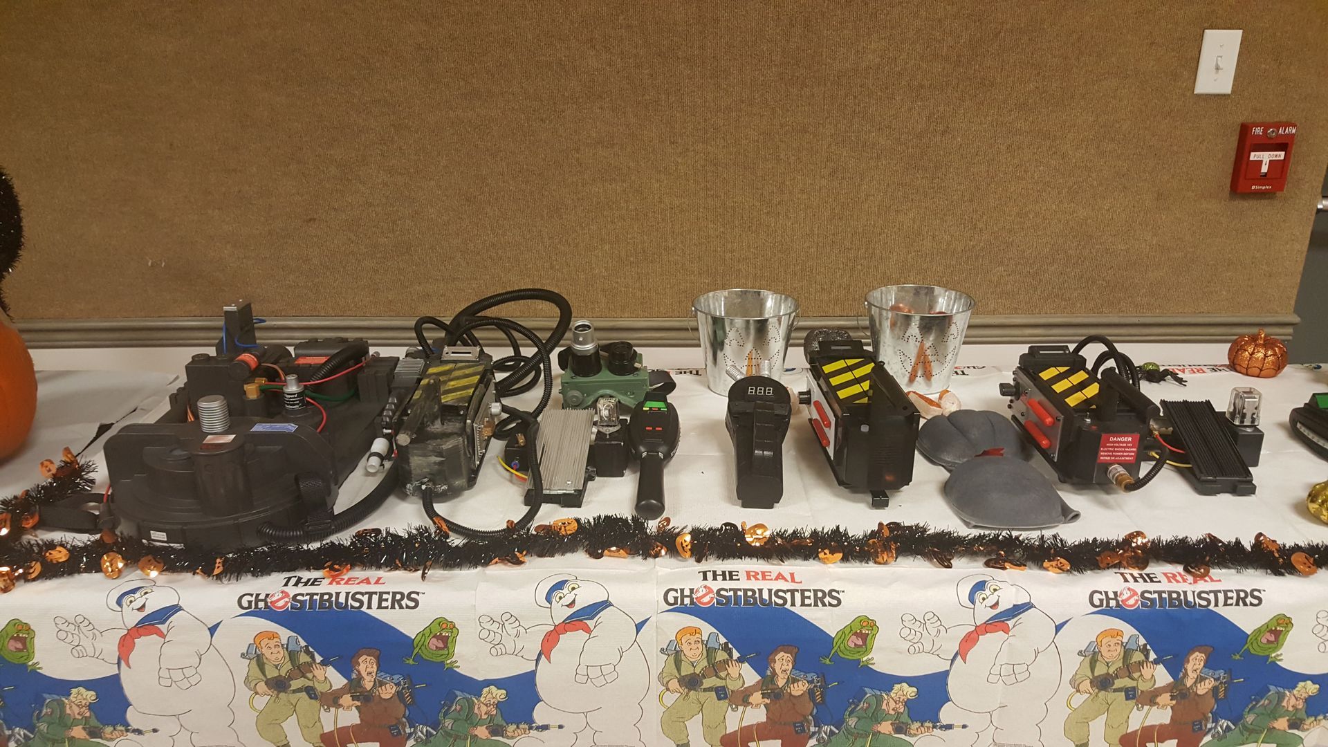 Table covered with assorted electronic devices and wires, displayed along a wall with a holiday-themed tablecloth.