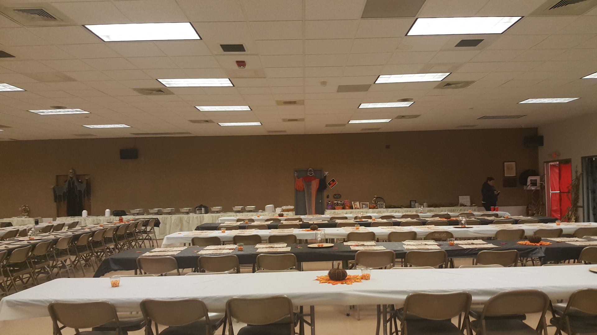 Empty banquet hall with rows of tables and chairs under bright ceiling lights.