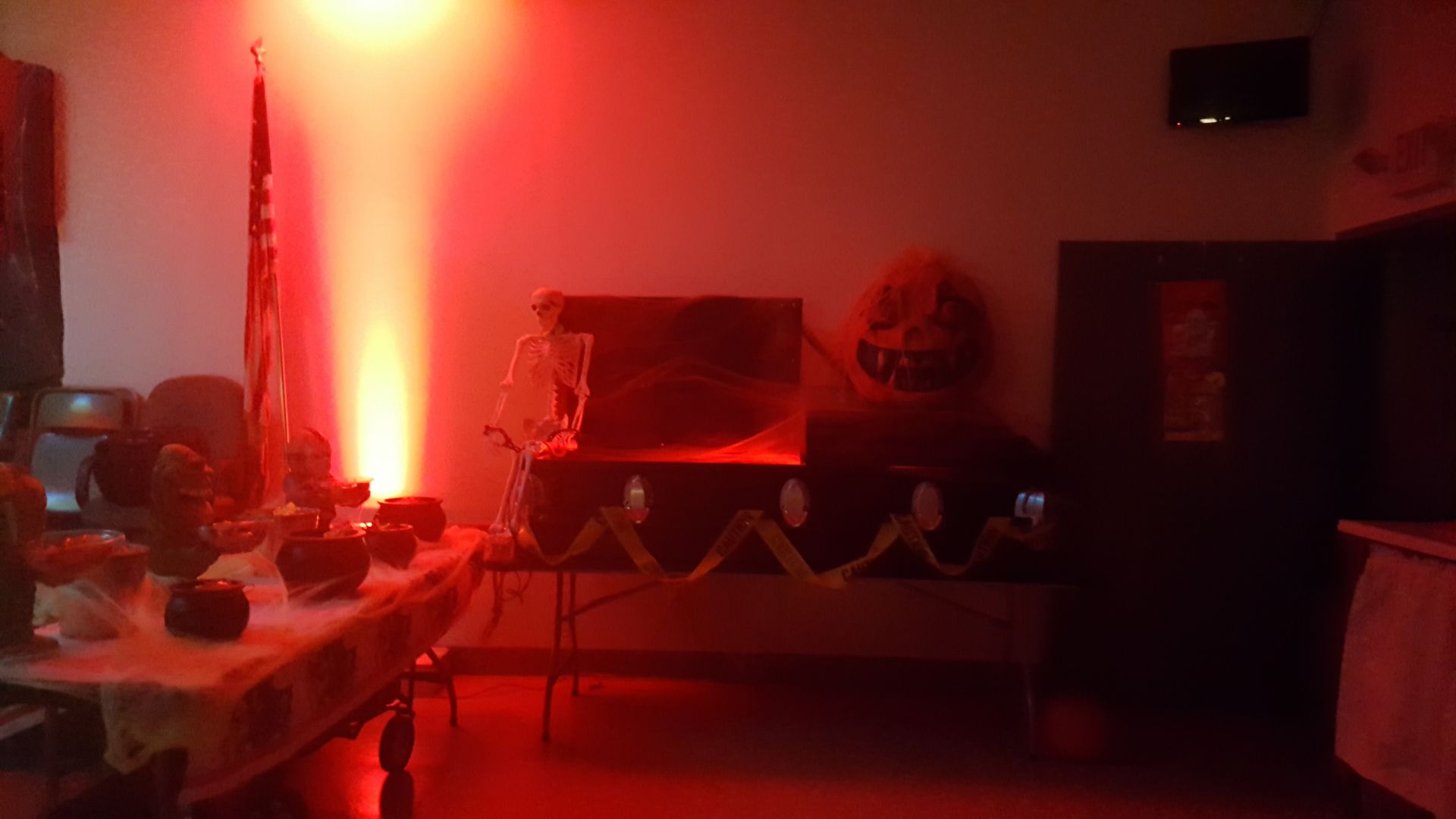 Dimly lit living room with red ambient lighting, a TV on a stand, and scattered furniture.