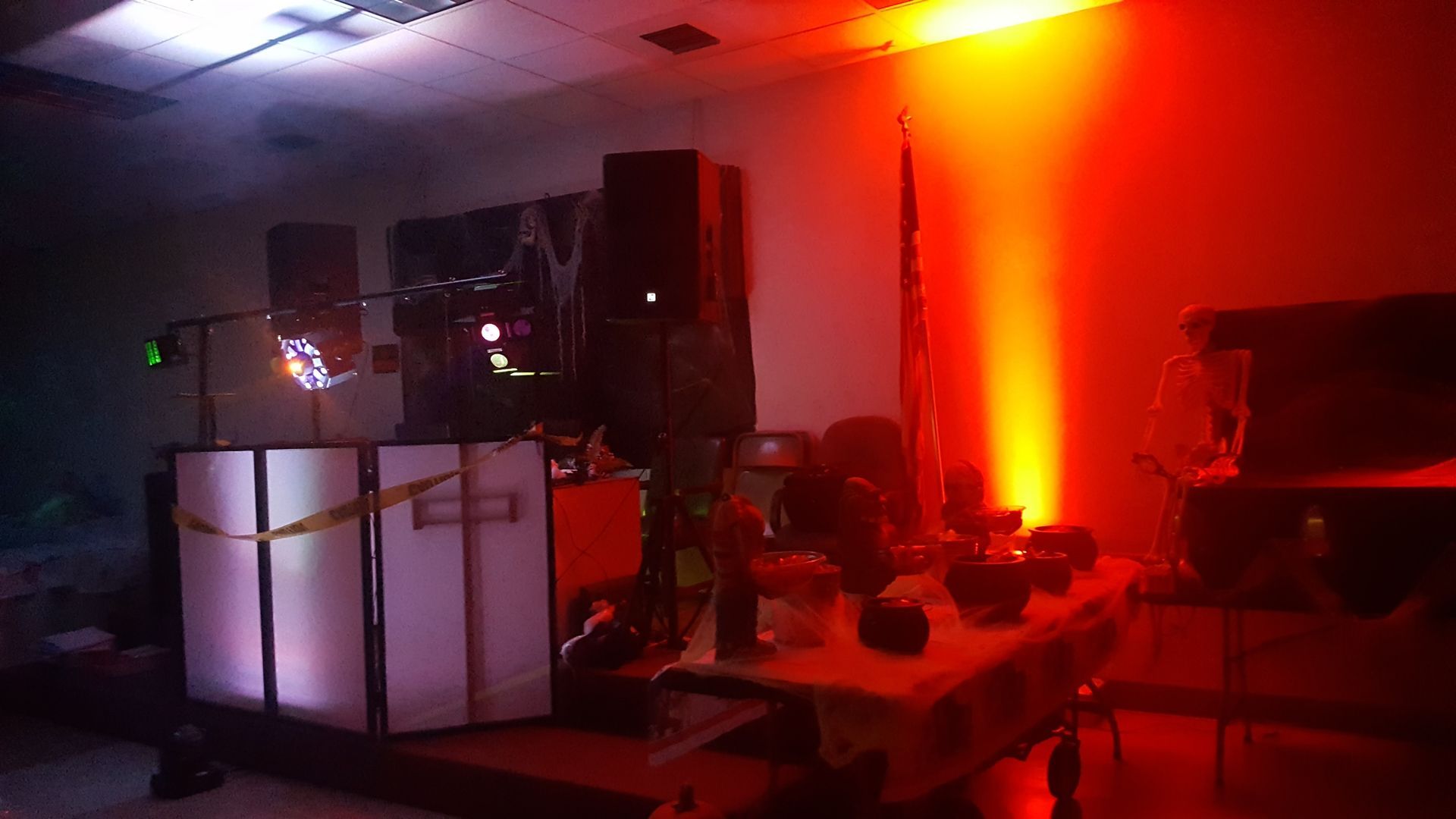 Dimly lit room with red-orange lights, equipment stands, speakers, and people seated at a table.