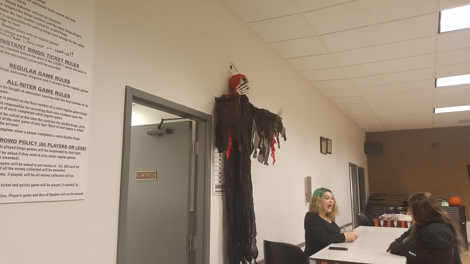 Hallway with a hanging Halloween decoration and people seated at a table near open doors