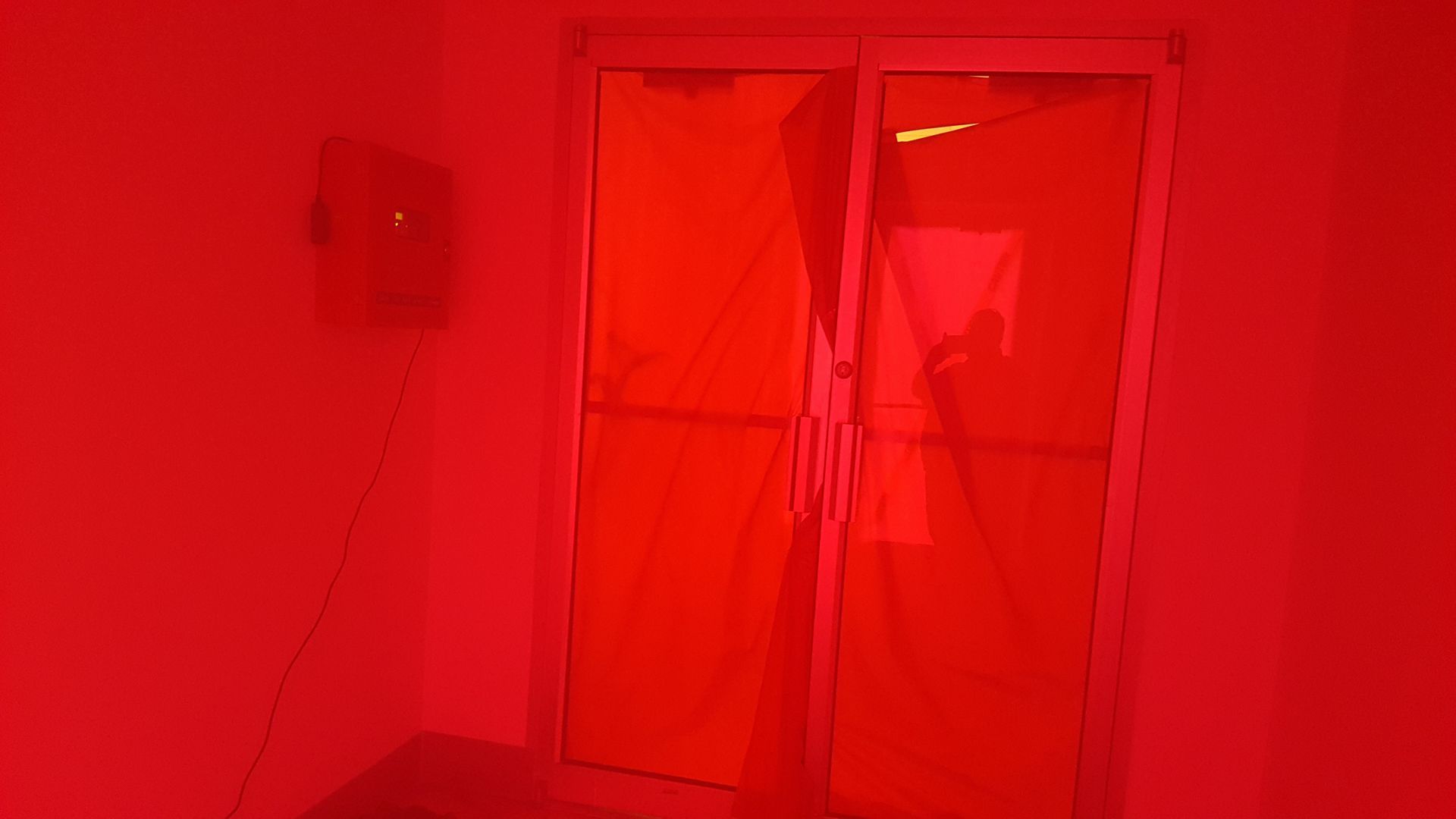 Red-lit room with glass double doors and a wall-mounted box on the left.