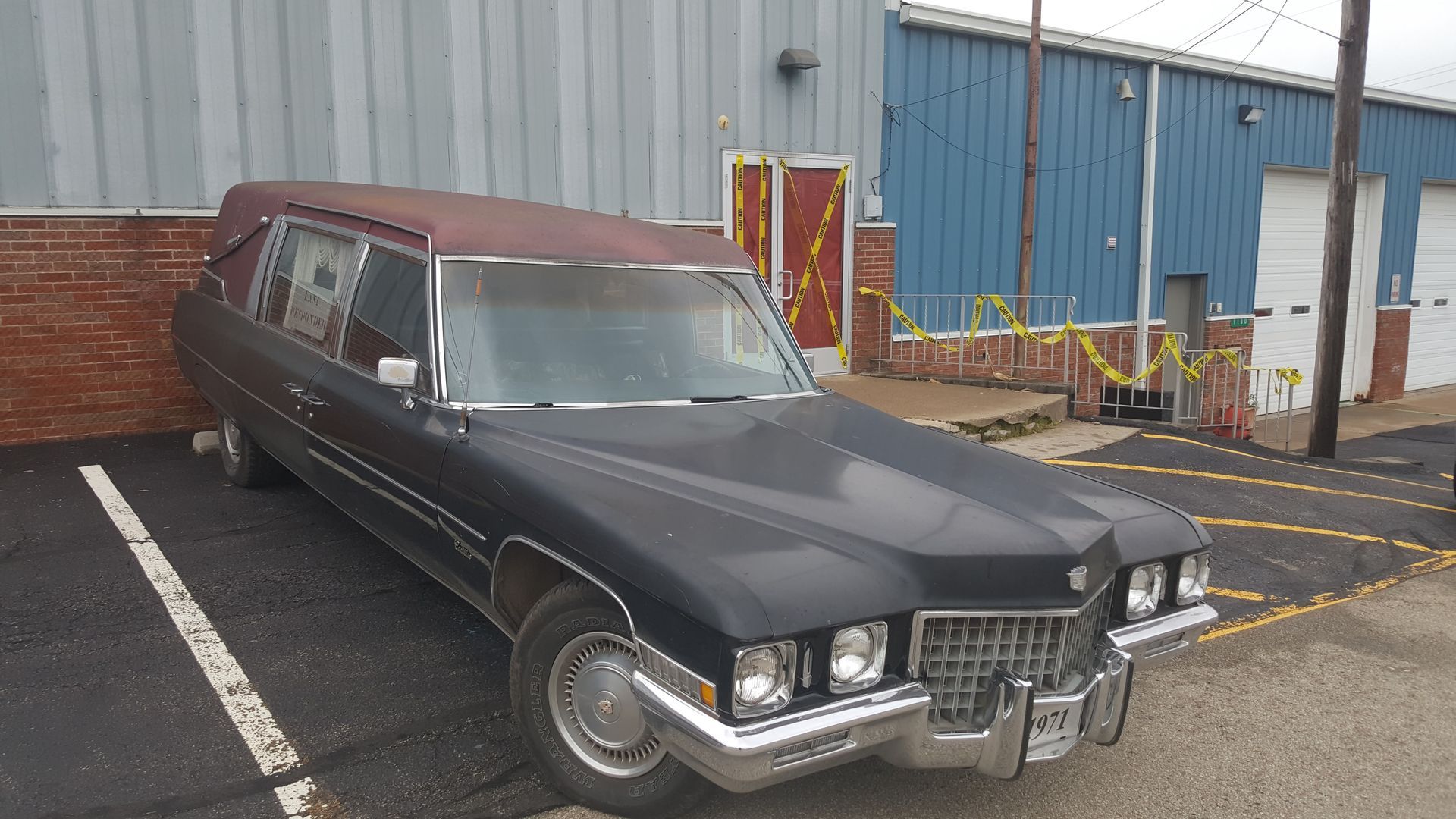 Black vintage hearse parked outside an industrial building in a striped parking space