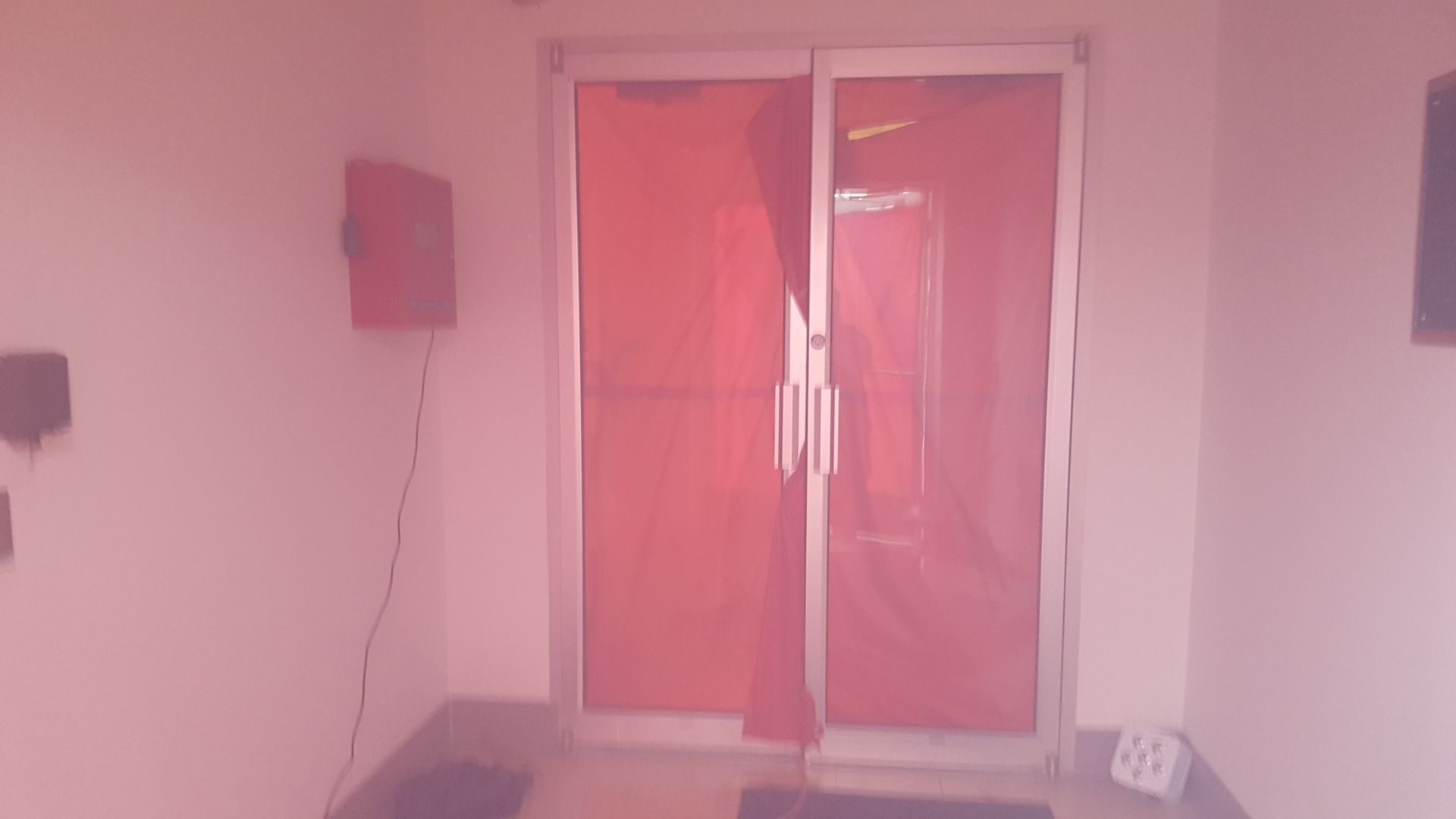 Pink-tinted room with red-framed glass doors and a wall-mounted device on the left