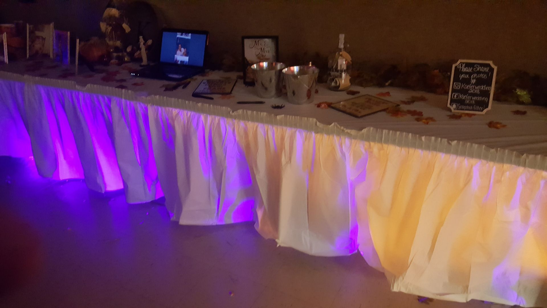 Decorated buffet table with purple and warm uplighting, white draped skirt, and party items on top