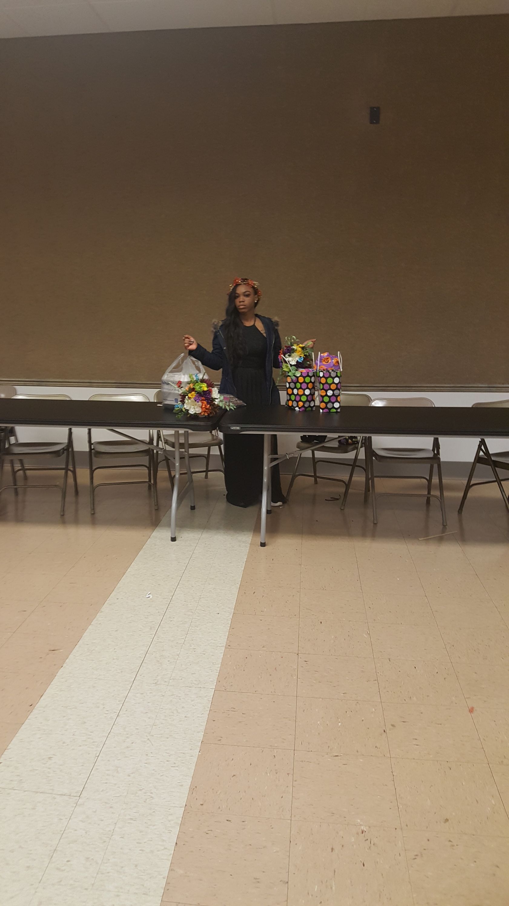 Person standing behind a long table in a hall, with colorful balloons and decorations on both sides.