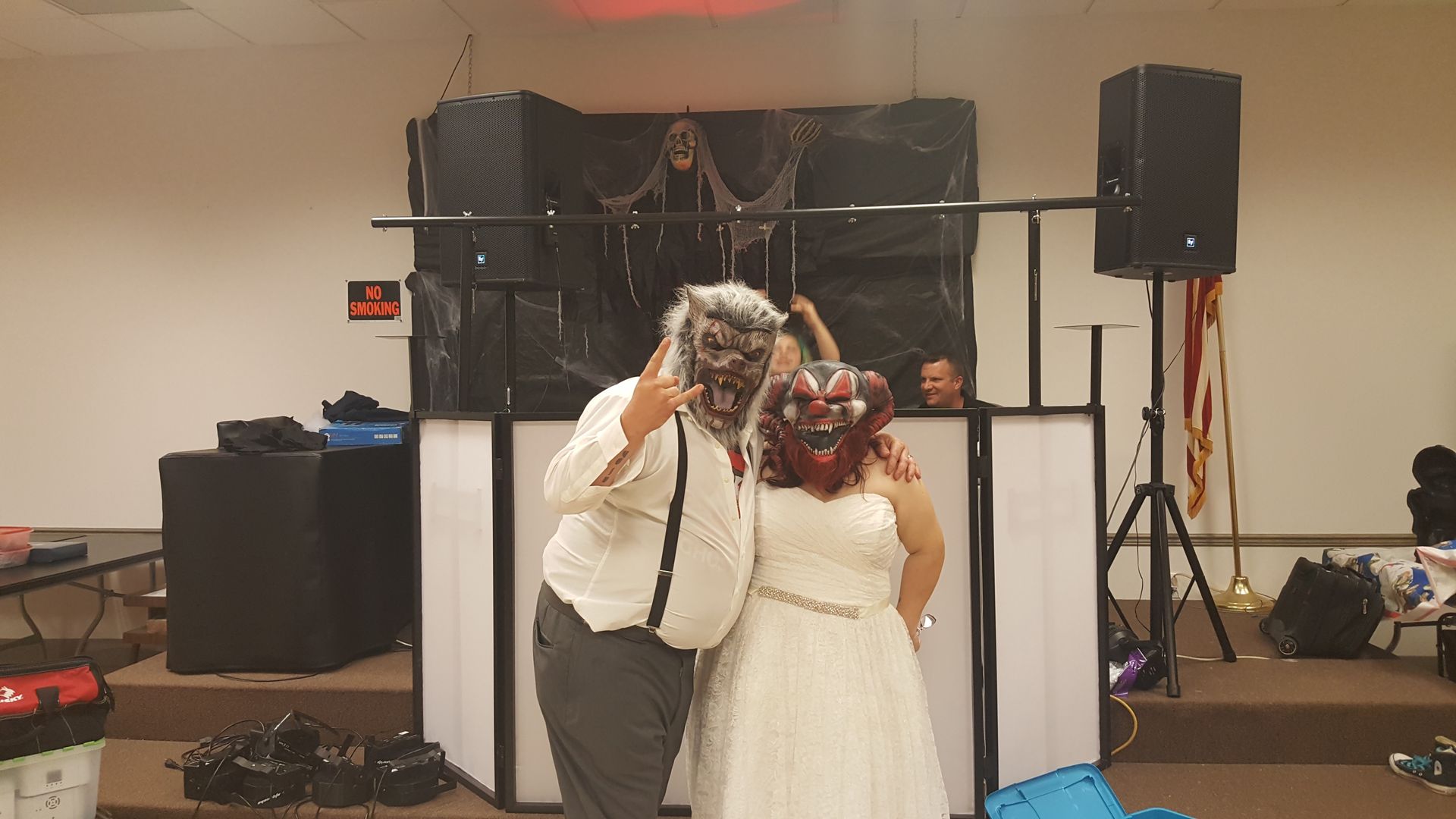 Couple in formal attire posing for a selfie at a decorated indoor event with speakers and a black backdrop