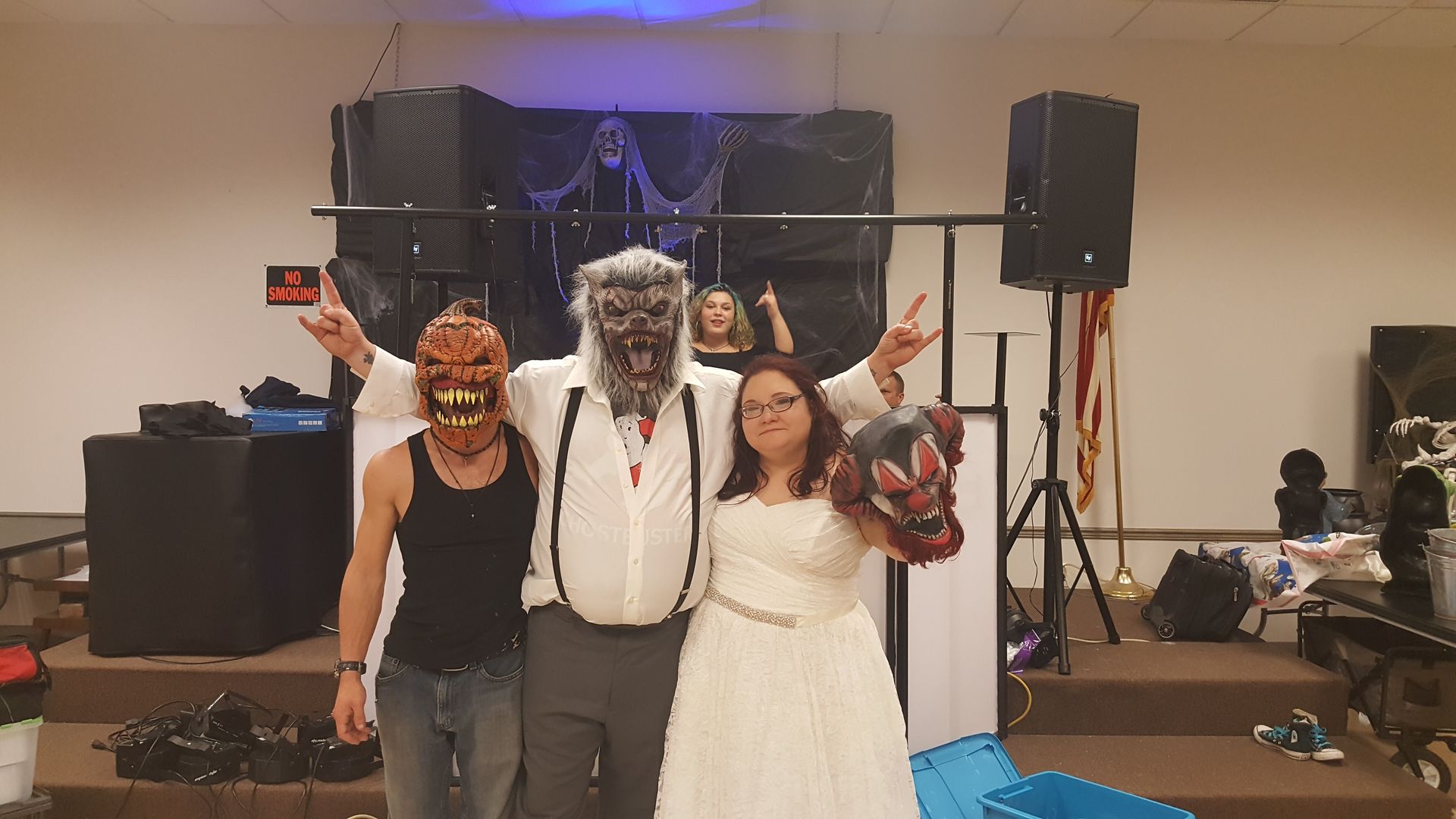Three costumed people posing on a stage with speakers and Halloween decorations