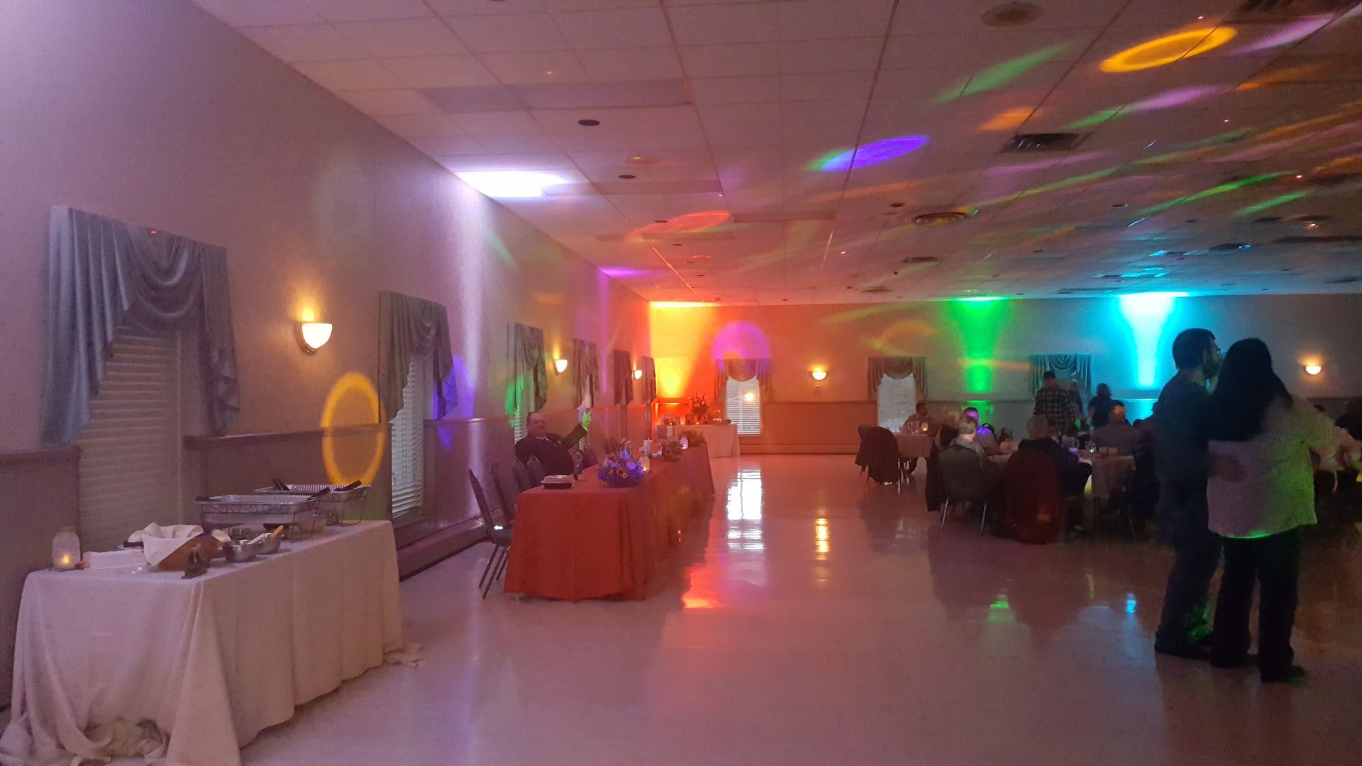 Decorated banquet hall with guests, colorful lighting, and buffet tables at an event