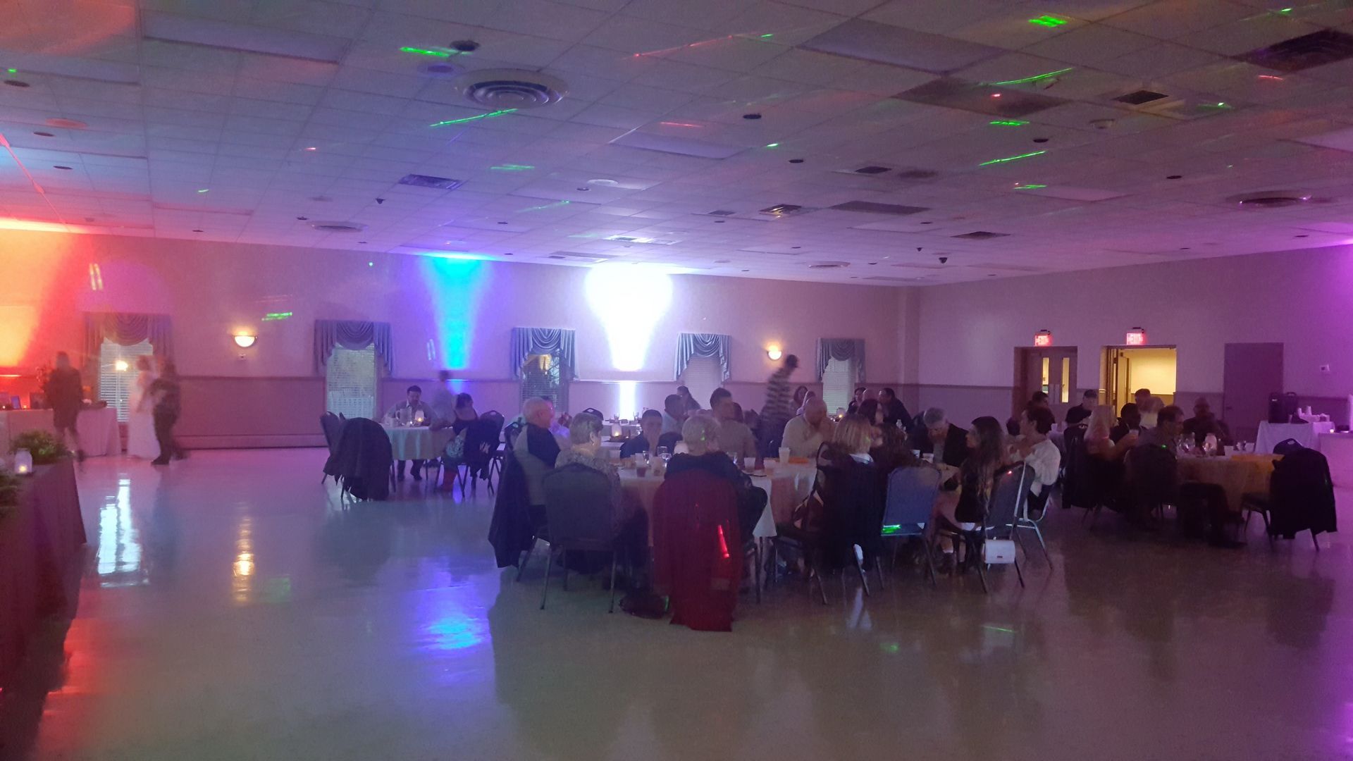 Banquet hall with guests seated at round tables under colorful purple and blue lights