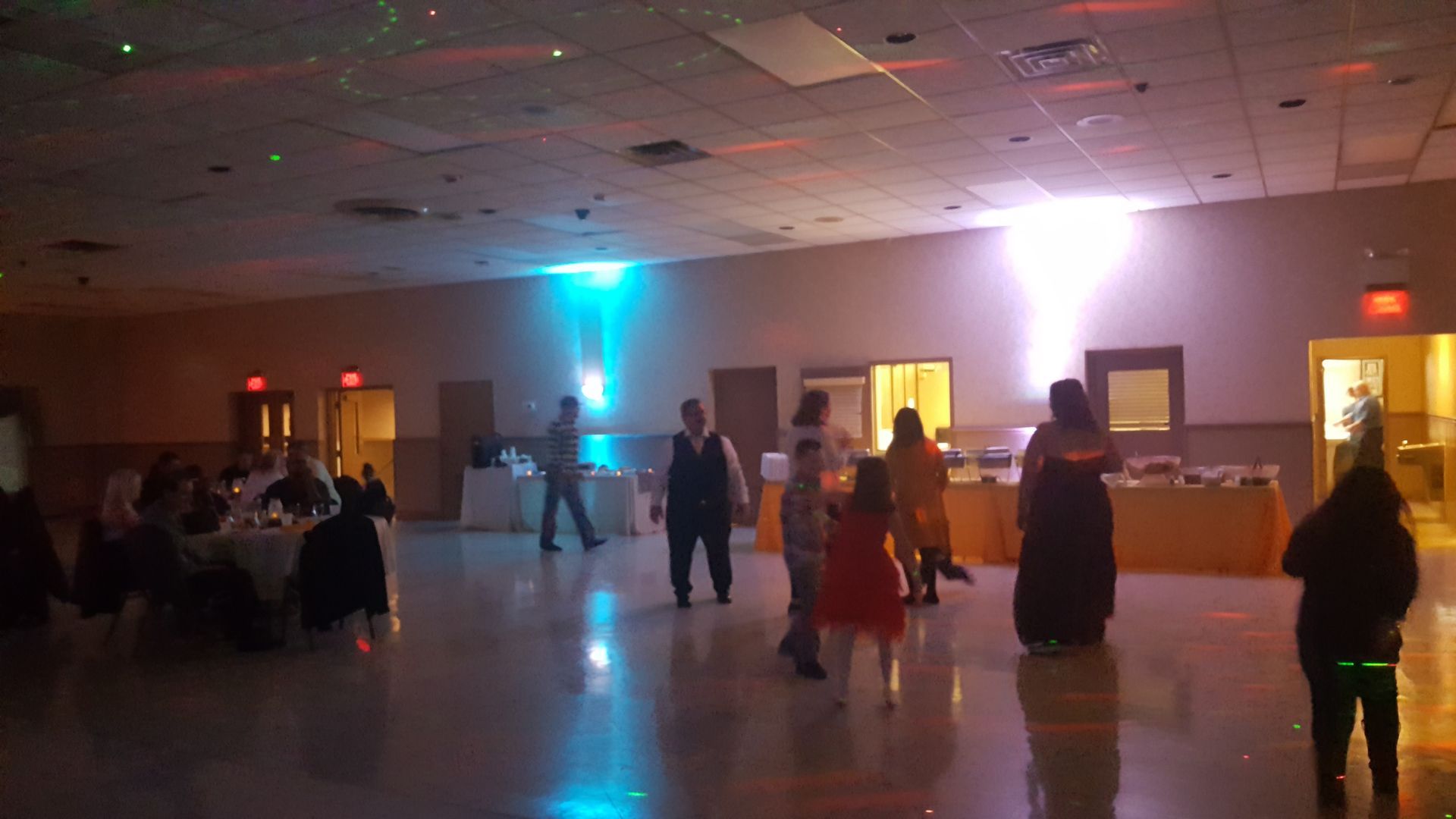 People dancing in a dimly lit hall with blue and pink lights during an indoor event