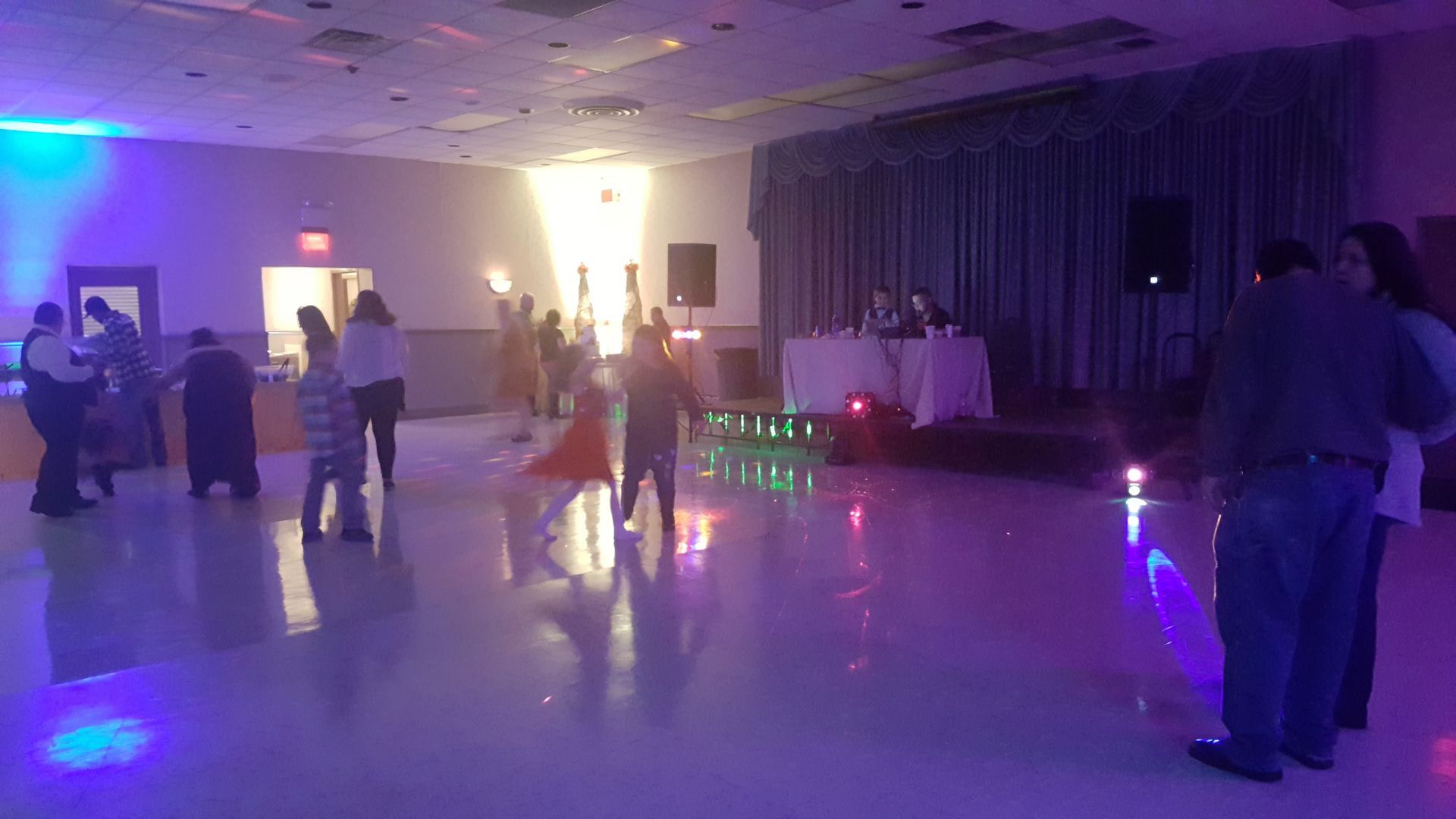 People dancing at a dimly lit party hall with purple and blue lights reflecting on the floor